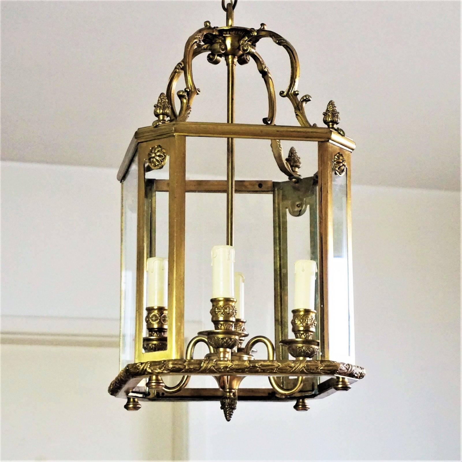 Large French Art Deco brass four-light lantern with bronze ornaments and eight glass windows, circa 1940.

European wiring: Four candle covers with E14 light sockets

Measures: Total height 42 ½ in / 108 cm
Height without hanging chain 20 ¾ /
