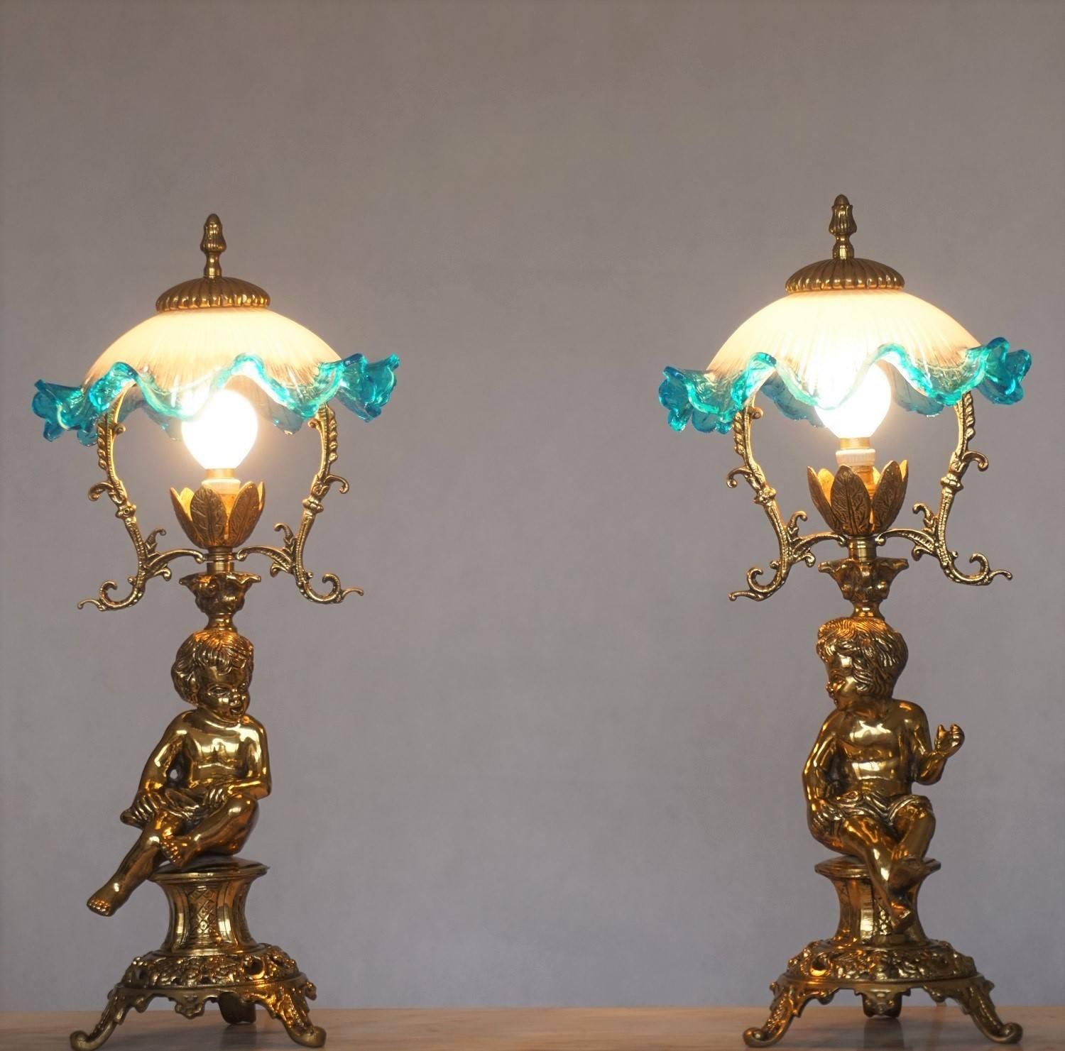 Pair of solid brass cherub table lamps Art Nouveau style, raised on richly ornate plinth base, with large glass flower lampshade, circa 1920.

One lamp socket
Measures: Height 19.75 in (50 cm)
Diameter 9.50 in (24 cm)
Base D 6 in (15 cm) 

Please