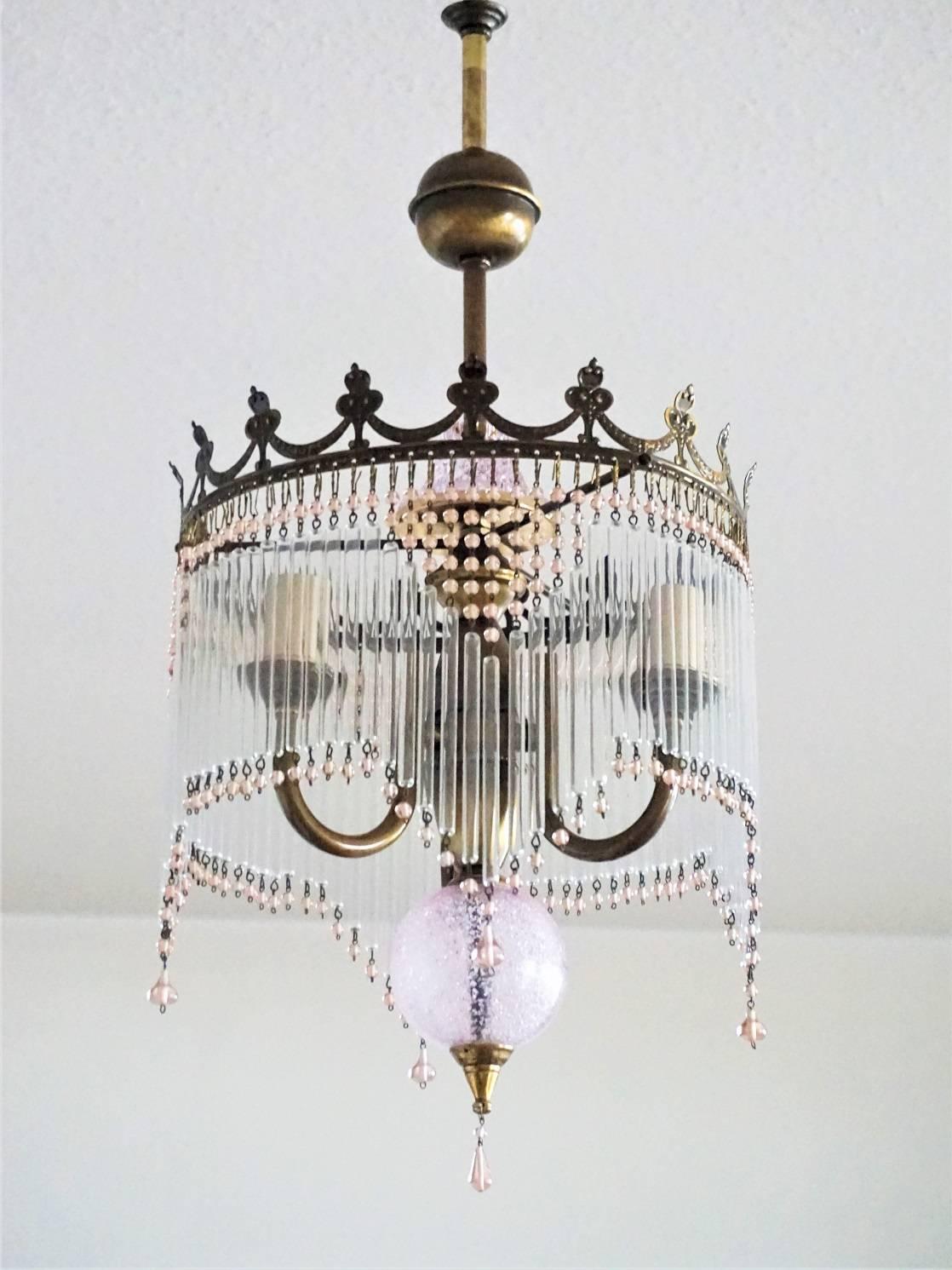 Lovely Art Nouveau style brass three-light chandelier with glass rods and rose colour glass pearls - impressive lighting effect!

European wiring: Four E14 bulb sockets 
Measures:
Total height 28.75 in (73 cm)
Diameter 11 in (28 cm).
 