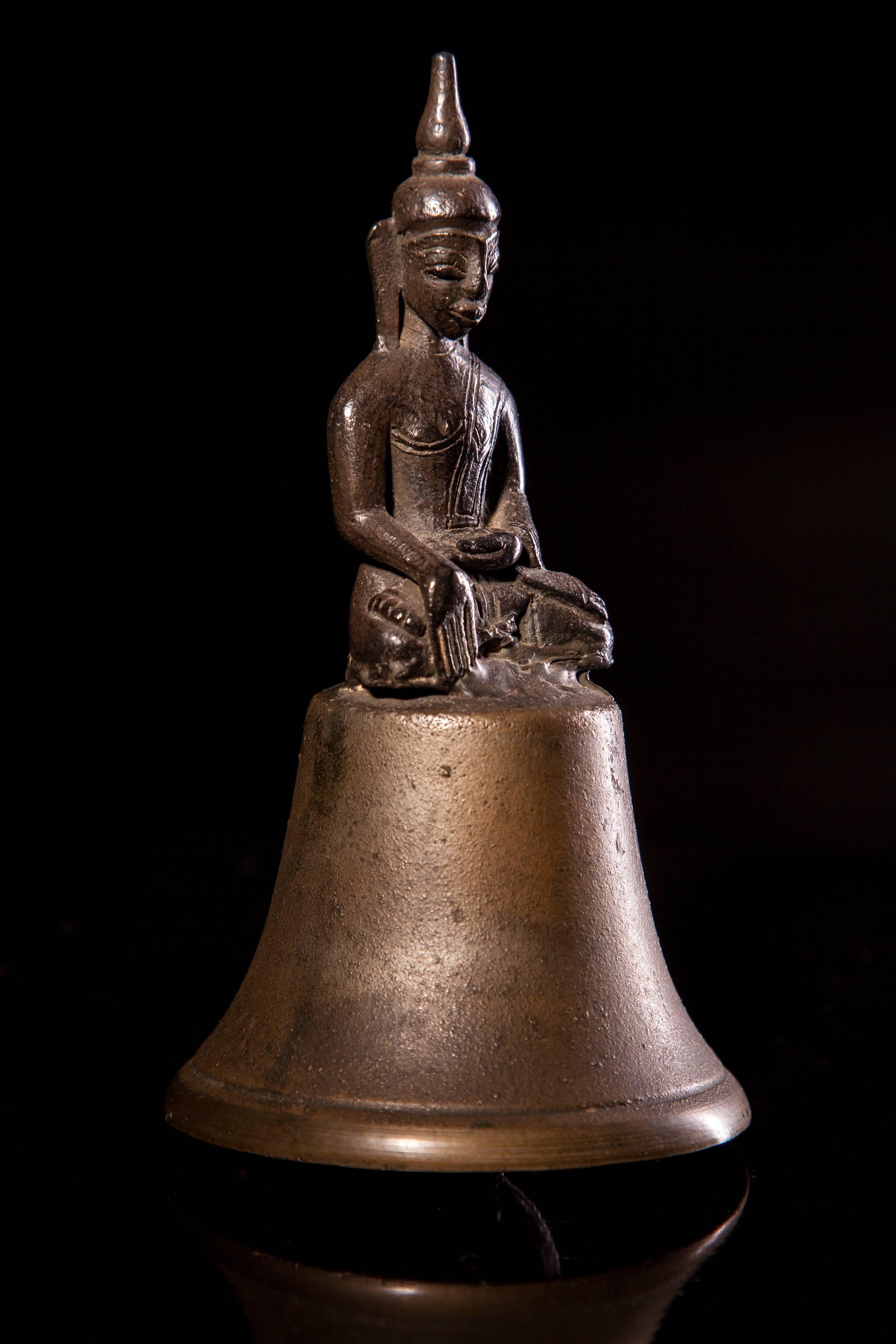 Burma, Tai Yai (Shan States)
18th-19th century 
H. (Overall) 14.5 cms, 5 ¾ ins
H. (Buddha only) 8.5 cms, 3 3/8 ins
Attached to an old brass bell, perhaps at a later date and possibly for use by a monk.
  