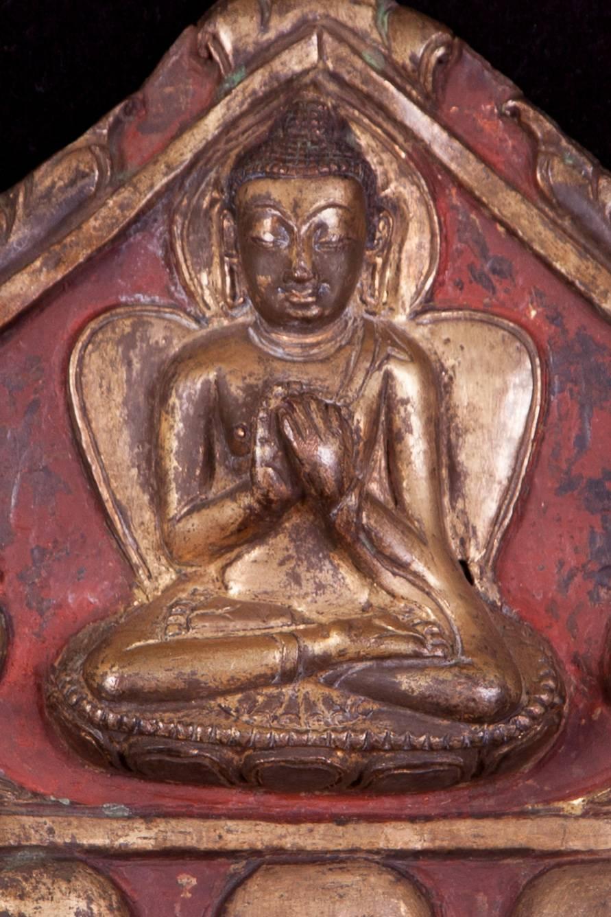 A delightful pair of gilded and painted repoussé copper plaques, once part of a larger shrine, each depicting a seated Buddha against a red background, his hands raised in dharmachakramudra (the gesture of ‘turning the wheel of the law’), with