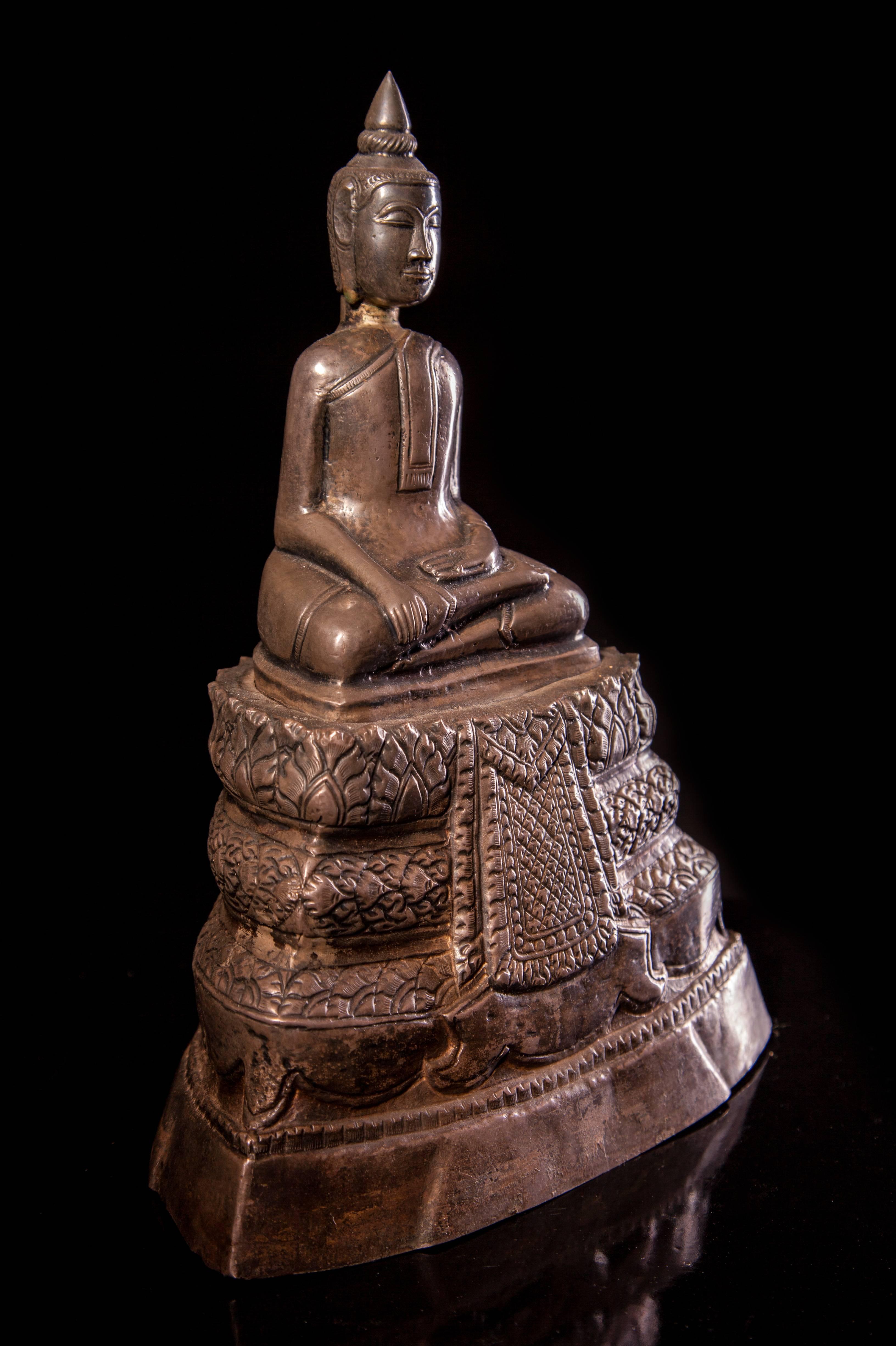 A silver figure of a seated Buddha on a stepped pedestal, the reverse with a dedicatory inscription
Cambodia,
19th century
Provenance: Private German collection.