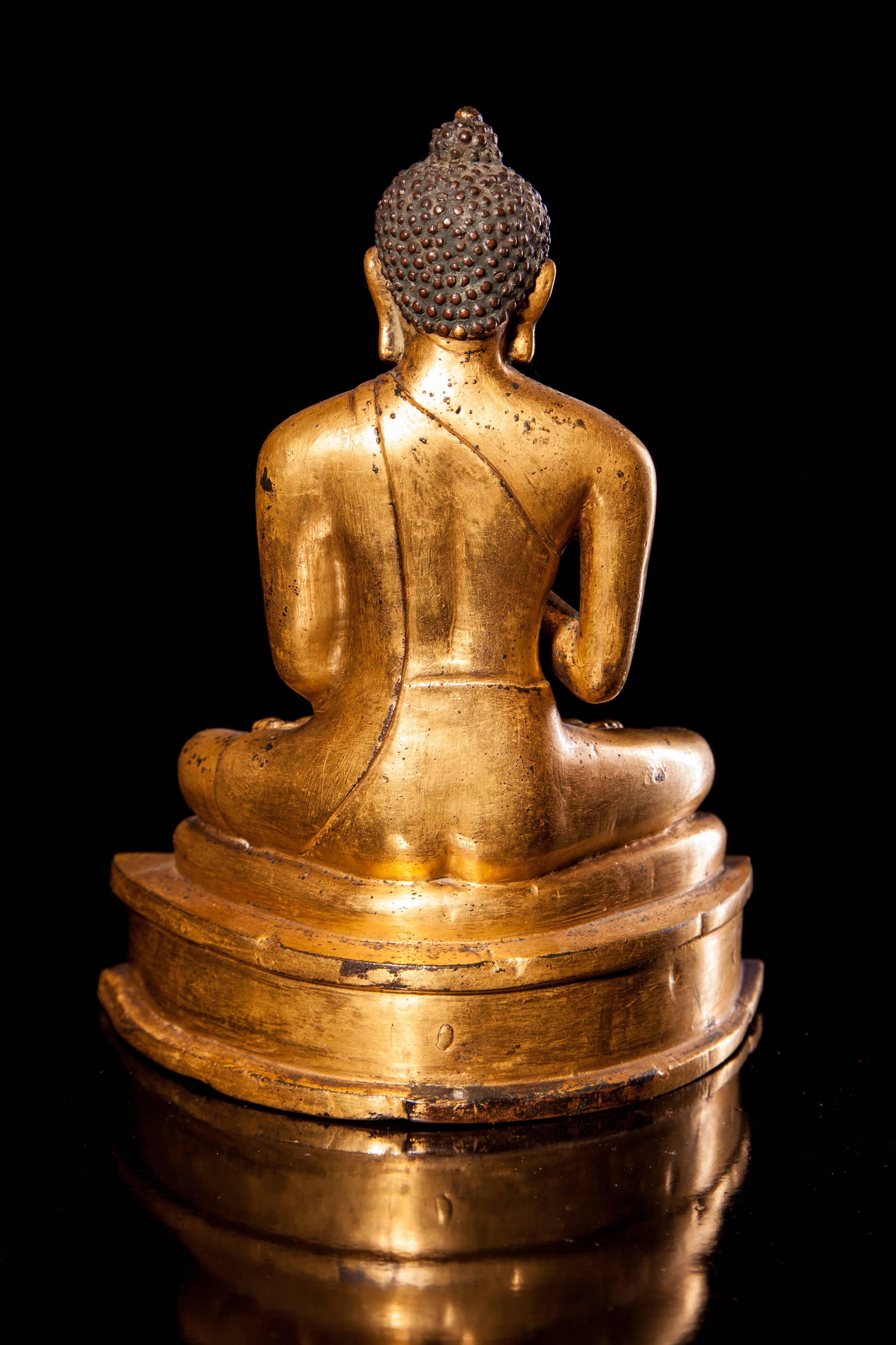 Cast seated in dhyanasana on a cushion supported on a waisted plinth decorated with three circles, the hands held in dharmachakramudra, the serene face with gentle smile and lidded eyes beneath arched brows centered by a raised Urne, flanked be