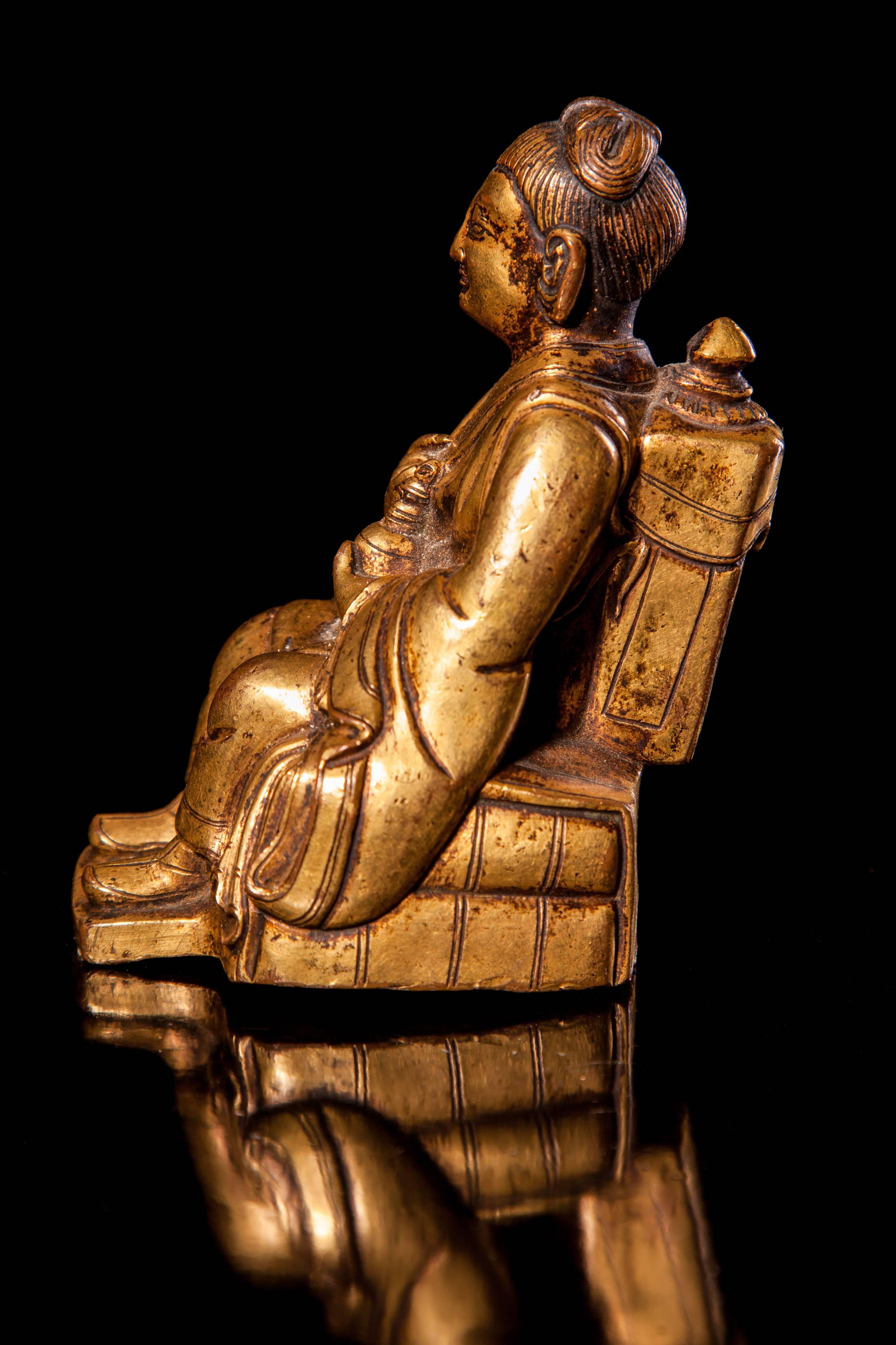 Seated in 'Royal Ease' on a pillow base, holding a fly whisk and bumpa, clad in long flowing robes, the face with heavy-lidded eyes, the hair pulled into a topknot, wearing a backpack, with a tiger on his right.
Measures: 3 7/8 in. (9.8 cm.) high.