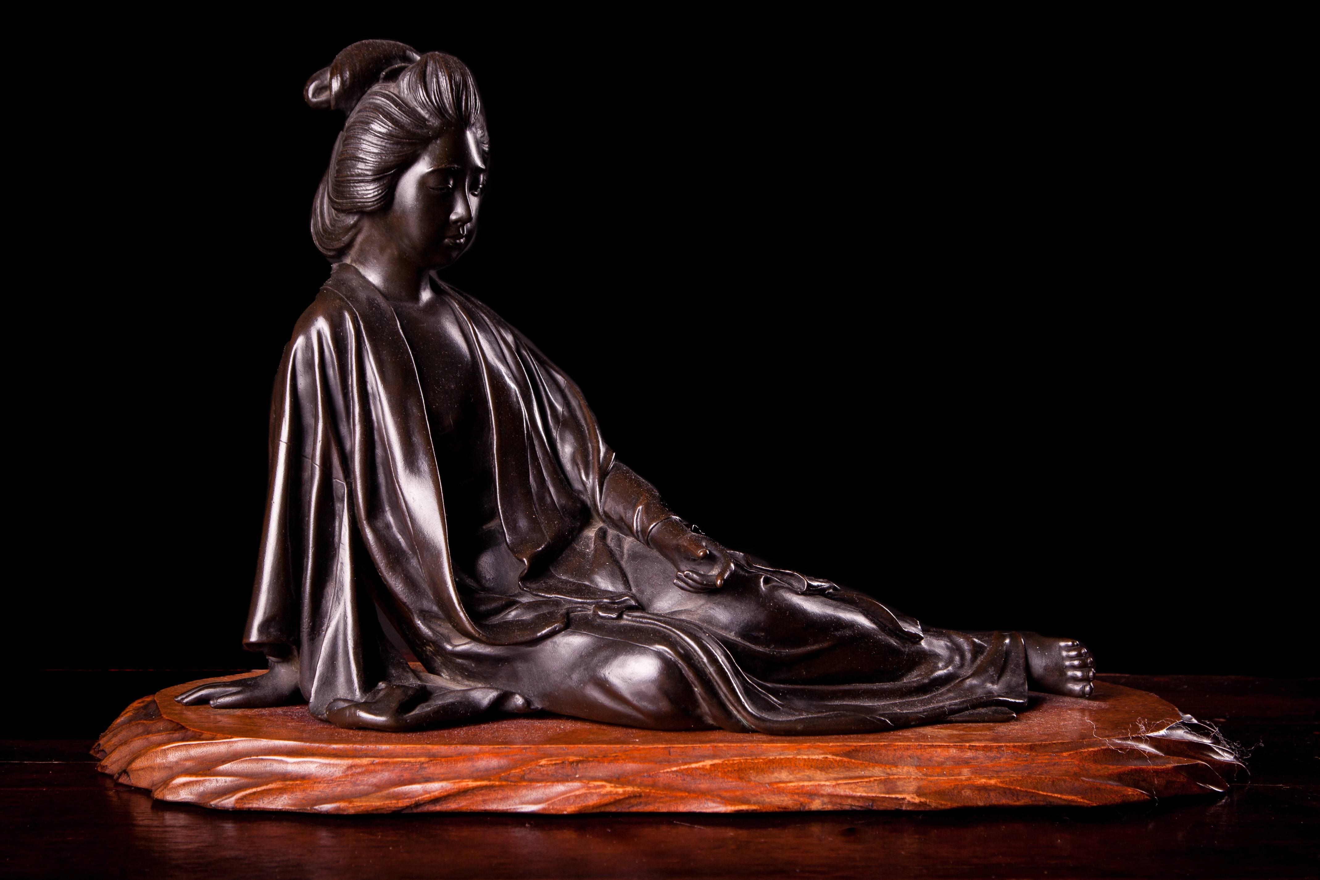 A Meiji bronze figurine of a reclining Japanese lady, her left hand on her left thigh with forefinger slightly extended, seal mark to base, wooden plinth
Measures: H 27 cms, W 36.5 cms
Provenance Malcolm Farley.