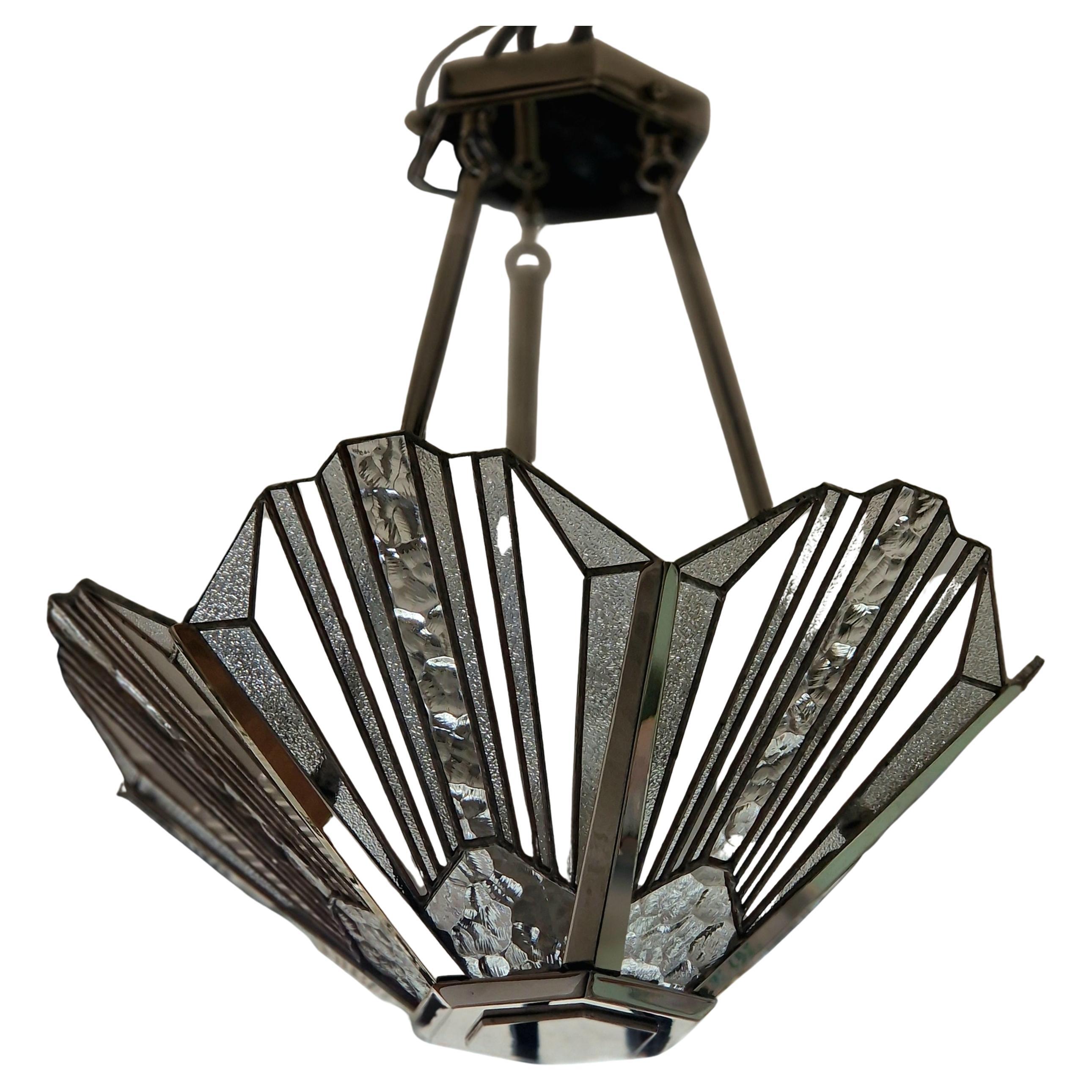 
An Art Deco chandelier in bronze with elegant lines, blending robustness and refinement. It features textured stained glass, arranged in perfect symmetry. The 1920s-inspired motifs create a unique play of light, evoking a warm and sophisticated