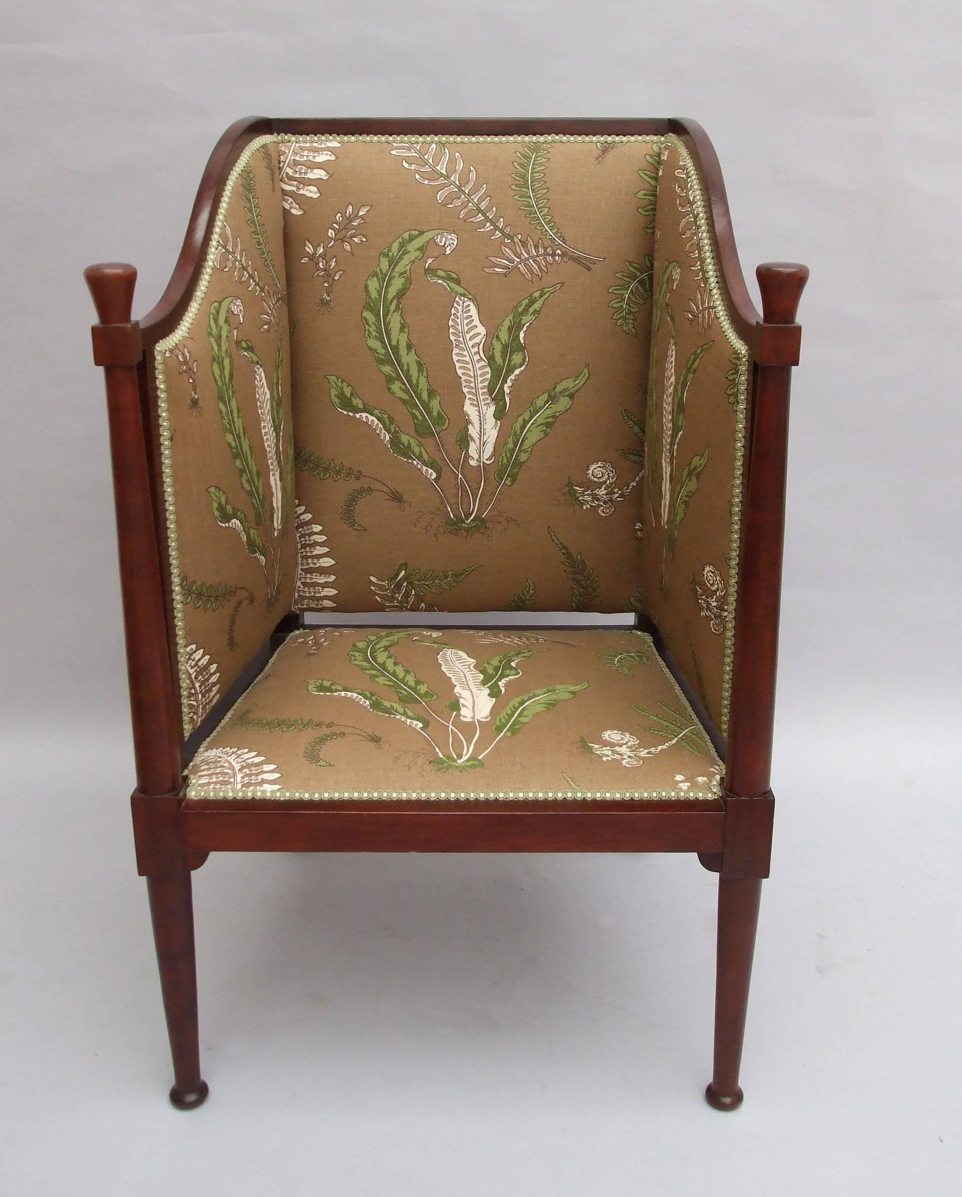 A mahogany Arts & Crafts high-sided wing chair with turned column front legs extended to finials, shaped sides, in the manner of Voysey, retailed by Liberty's, circa 1900, newly upholstered in fern pattern fabric, designed by Elsie de Wolfe,