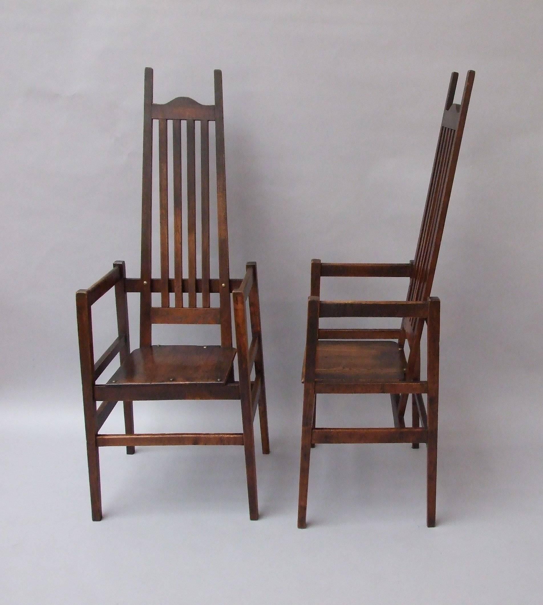C F A Voysey: A rare pair of oak armchairs with slats to the sloped tall backs and tall stiles either side. there are brass studs to the seats and the back rails, originally designed for The Homestead, Frinton-on-Sea, where both the house and the