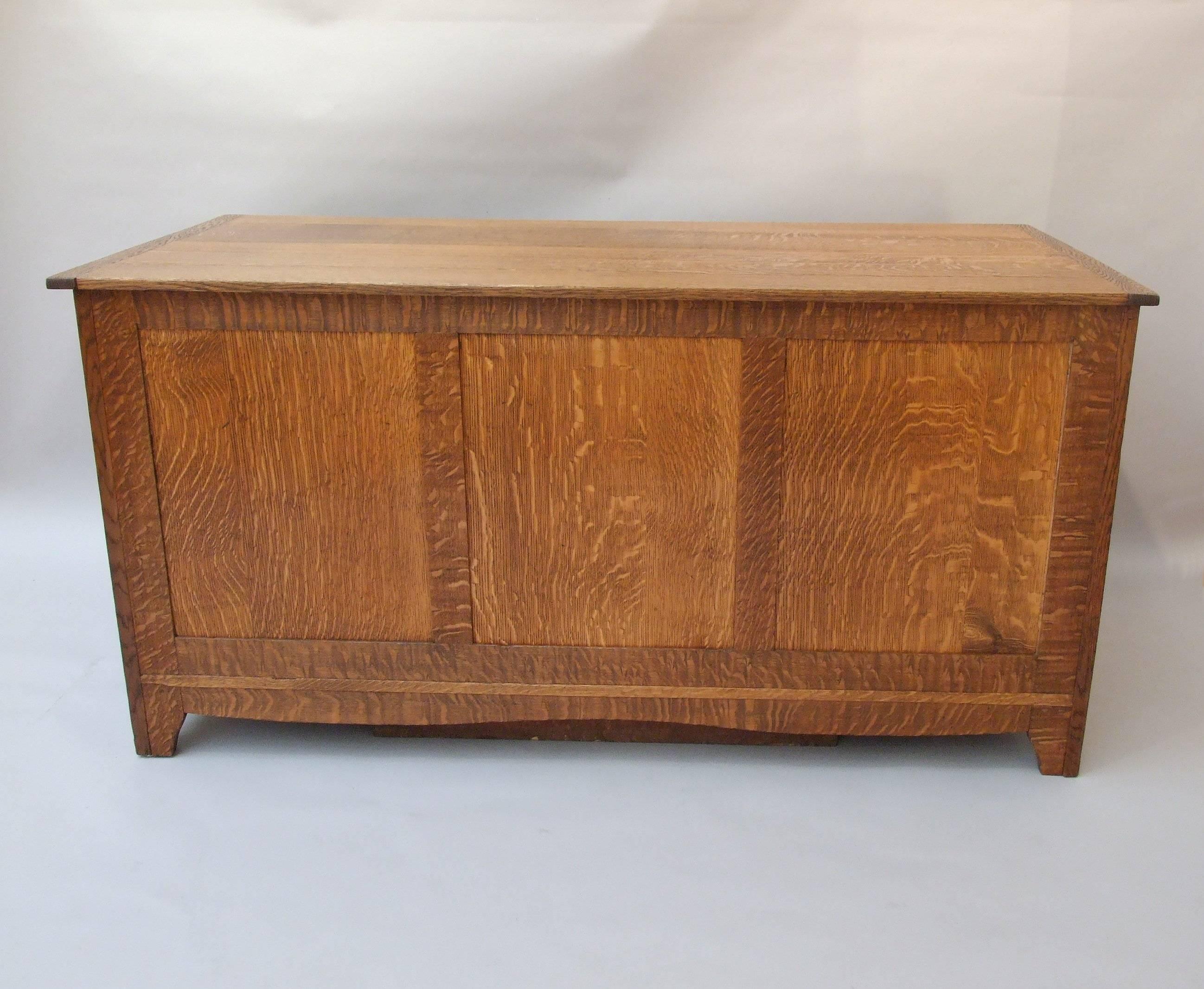 A rare, quarter-sawn, oak, freestanding desk with one long drawer between two short drawers over one deep drawer to each pedestal, pull-out slide to the top of each pedestal, panelled back, with shaped apron and legs, inset oval and nipped handles,