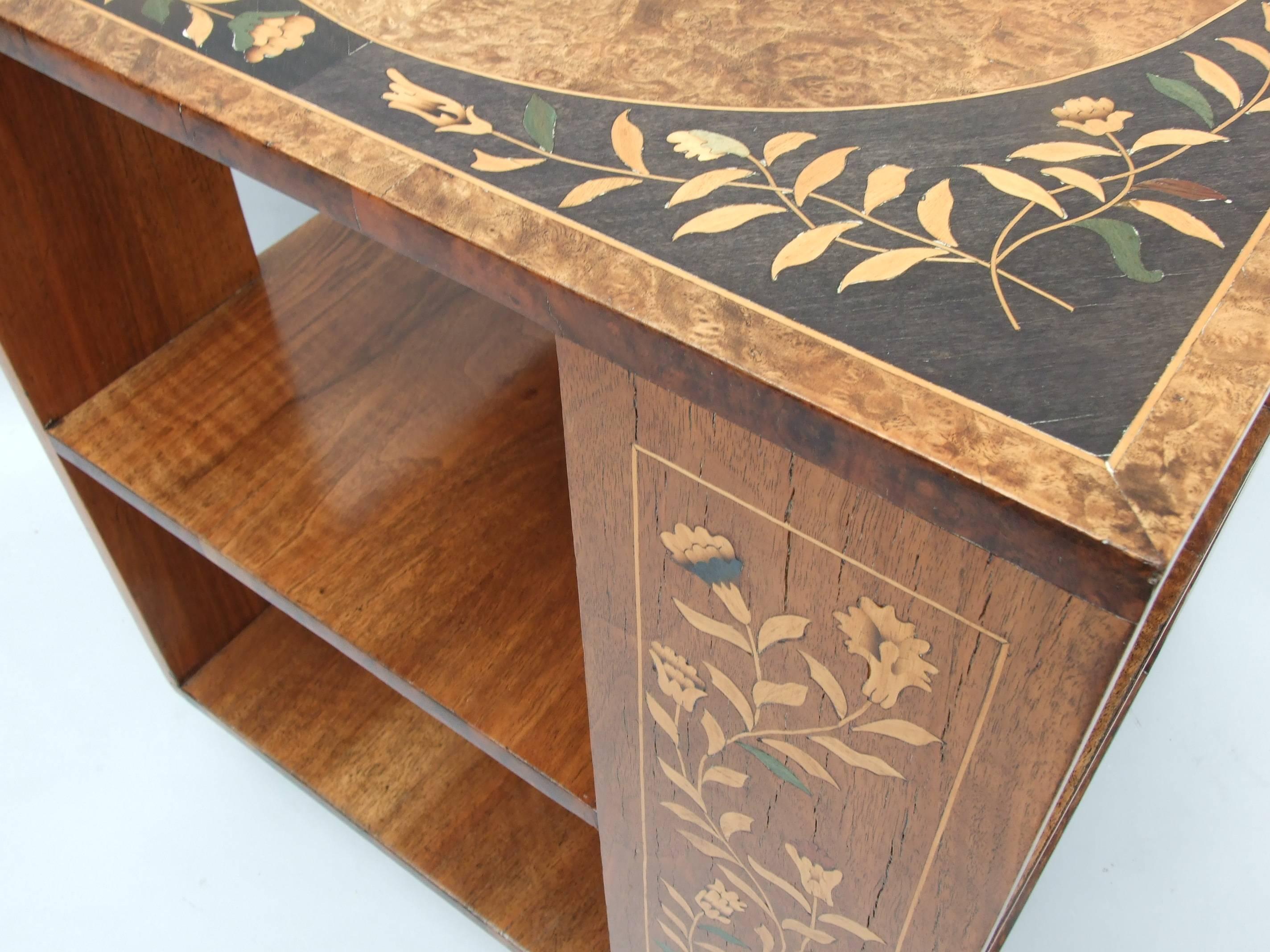 An unusual walnut booktable with extensive Fine floral marquetry inlay to the supports, the top with circular quartered burr walnut roundel with a surround of marquetry in ebony veneered panels, ebonised plinth, circa 1925, 61cm (24in) high, top