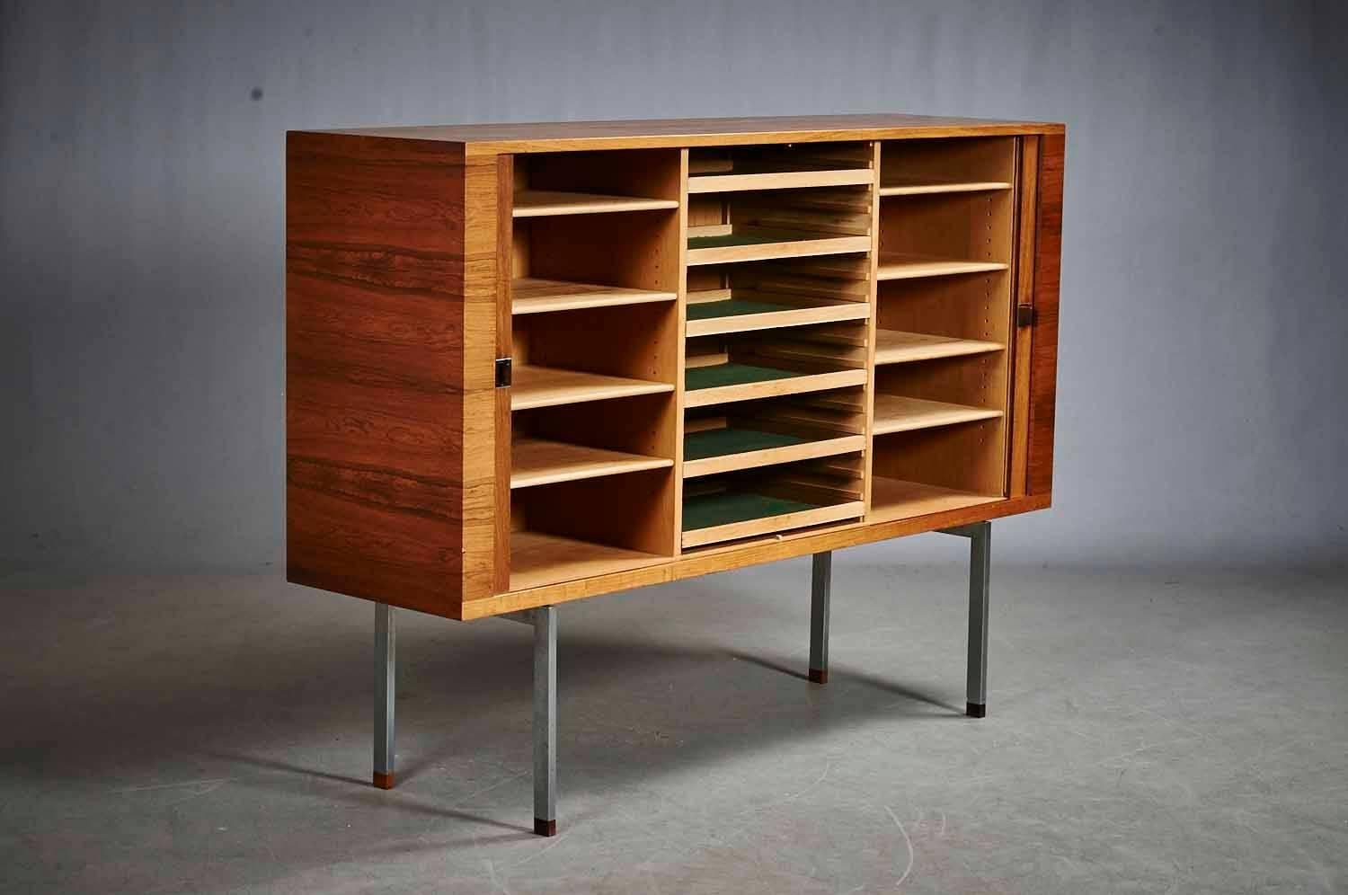 A large and rare “President” sideboard by Hans J. Wegner in rosewood and chrome metal made by Ry Mobler.

Sideboard in rosewood with two tambour doors enclosing shelves and sliding trays. Stainless steel handles and frame with rosewood leg ends.