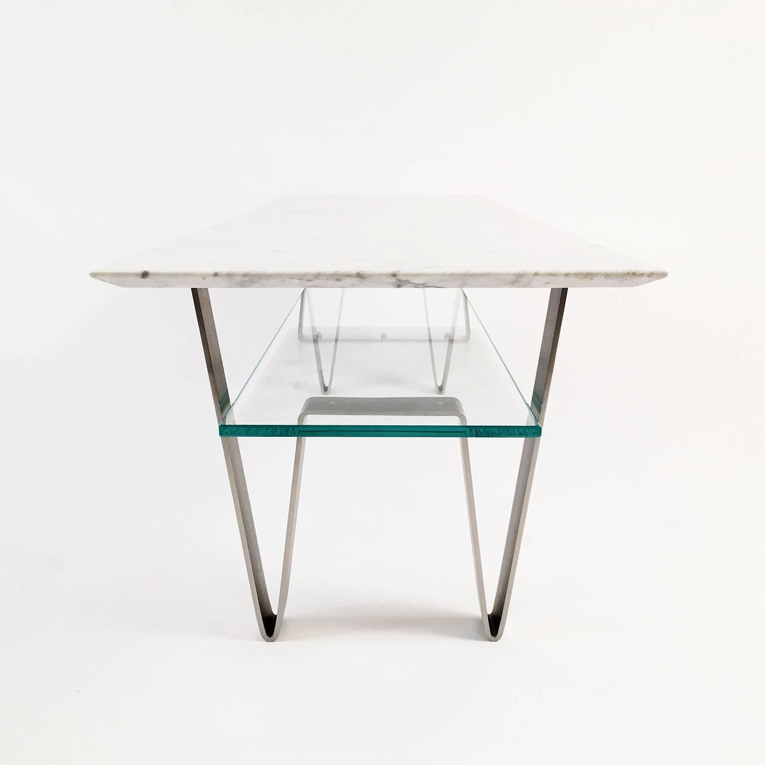 The Zaza table is a showpiece designed with display in mind. A Carrara marble top sits above a glass shelf for the presentation of books or objects. Both the marble and glass are supported by bent stainless steel hairpin legs - a contemporary nod to