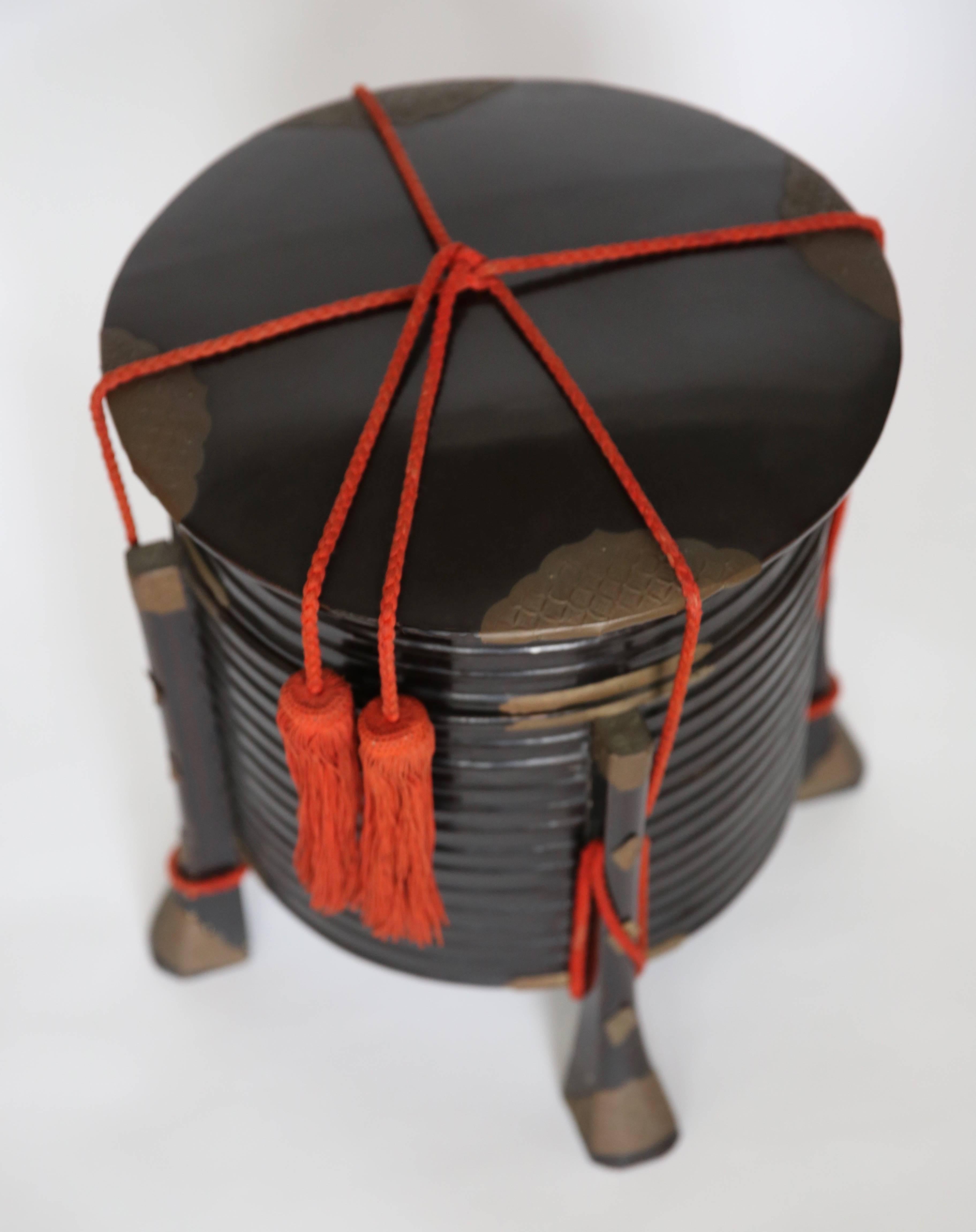 A Meiji period Japanese black lacquer hat box with red rope and chiselled copper decor details.
Japanese late Meiji period Hokkai box or hat box. 
The body shaped as a series of stacked rings. Four legs run up the sides of the body, and are