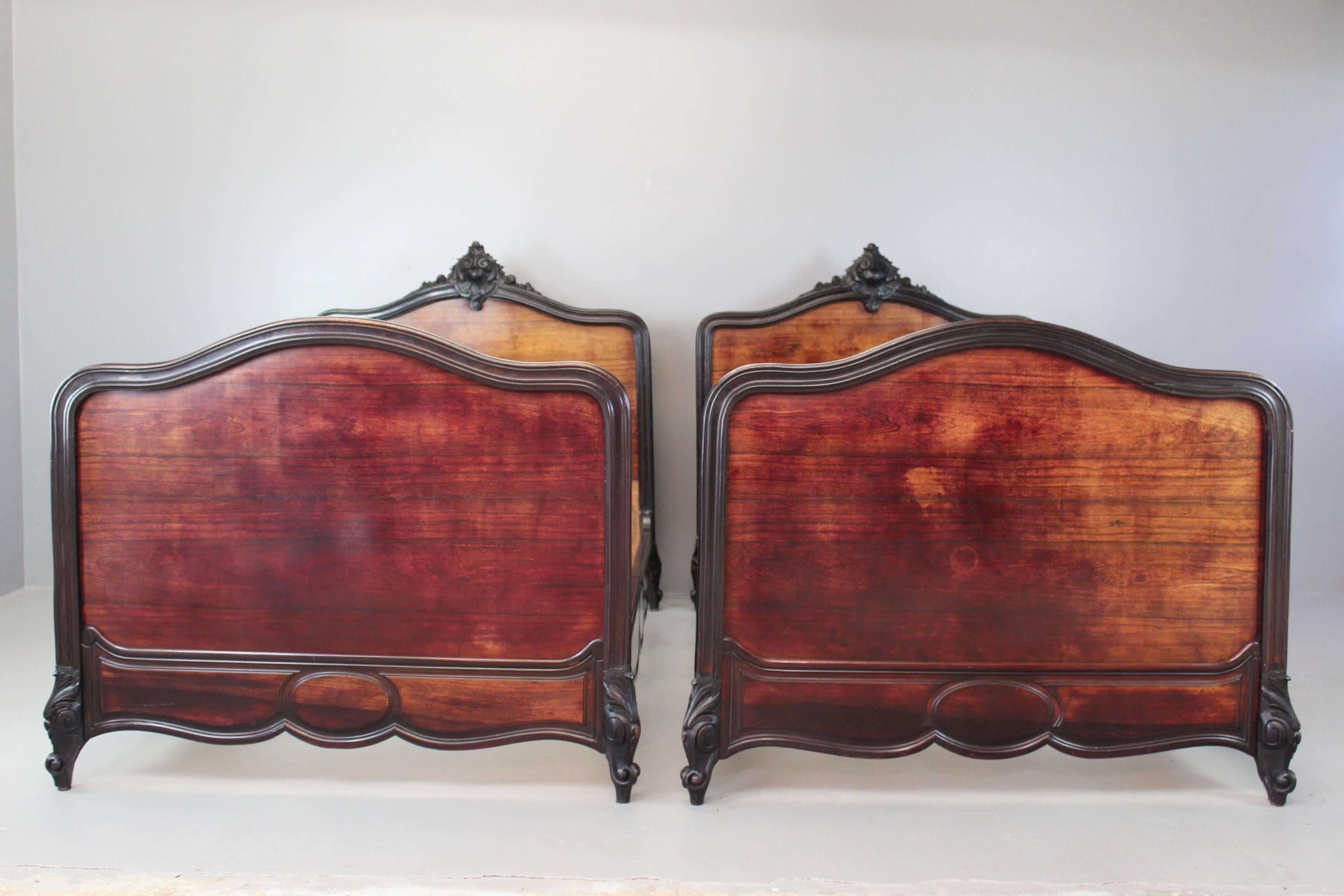 Beautiful pair of late 19th century French Louis XV style single beds. Each bed has an ornate carved crested ebonized frame, with a rosewood veneered head and footboard.

Please click our logo for more items, and to see our full inventory.