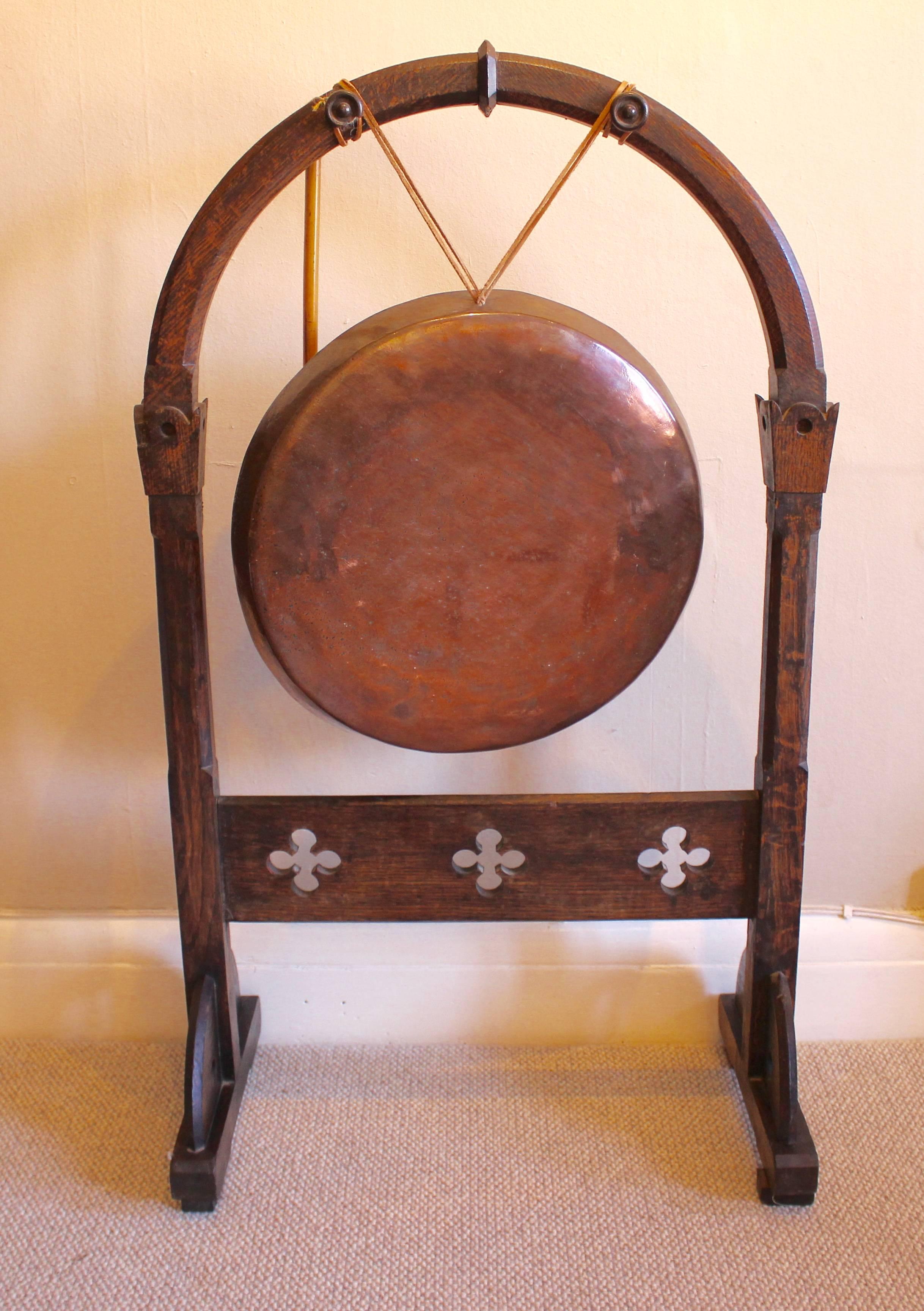 A large Victorian oak dinner gong with mallet. The large coppered bronze gong supported by leather ties to the arched oak frame. Having turned finials to support the gong. The foot of the arch is flanked by squared carvings above chamfered uprights