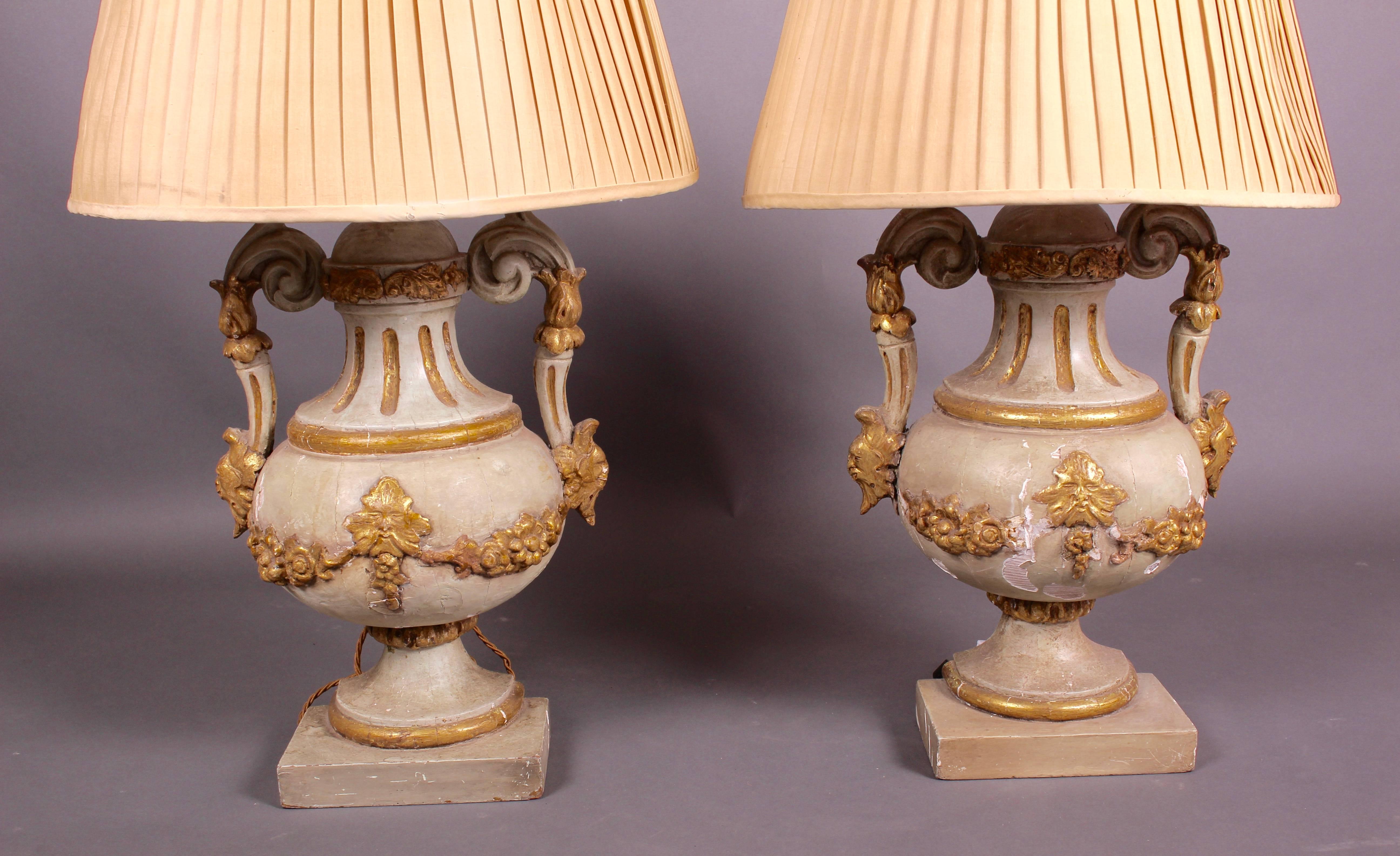 A large and imposing pair of Venetian urn lamps with pleated silk crescent-shaped shades. The urns with gadrooned neck and bulbous body, with gilded floral and mask decoration, probably that of Bacchus the Greek god of wine. Flanked by large