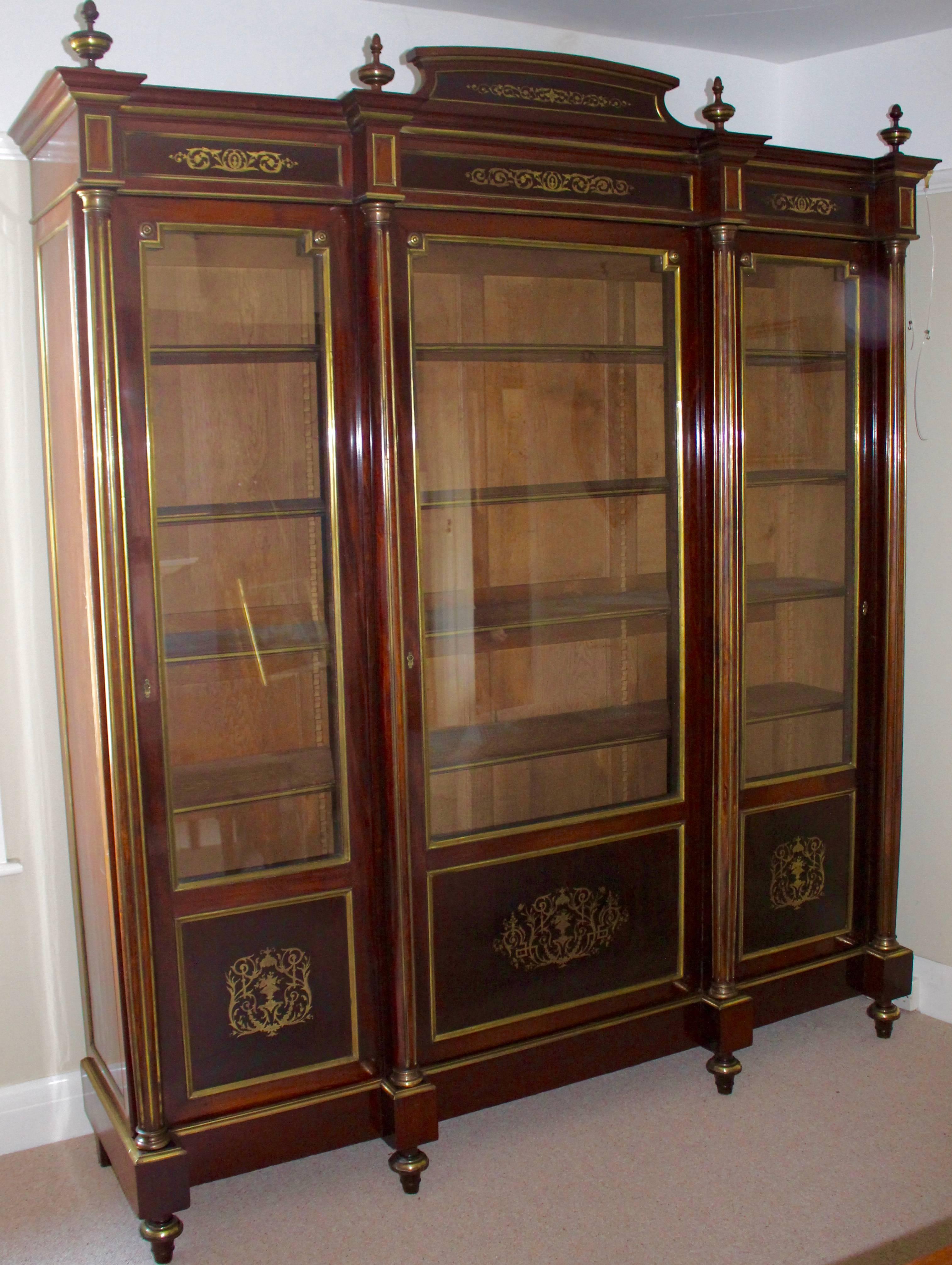 A large and exquisite 19th century French Mahogany and brass inlaid bookcase/display cabinet. Very attractive on the eye. Having central pediment between four turned finials with brass decoration. Above three glass panelled doors, each with brass