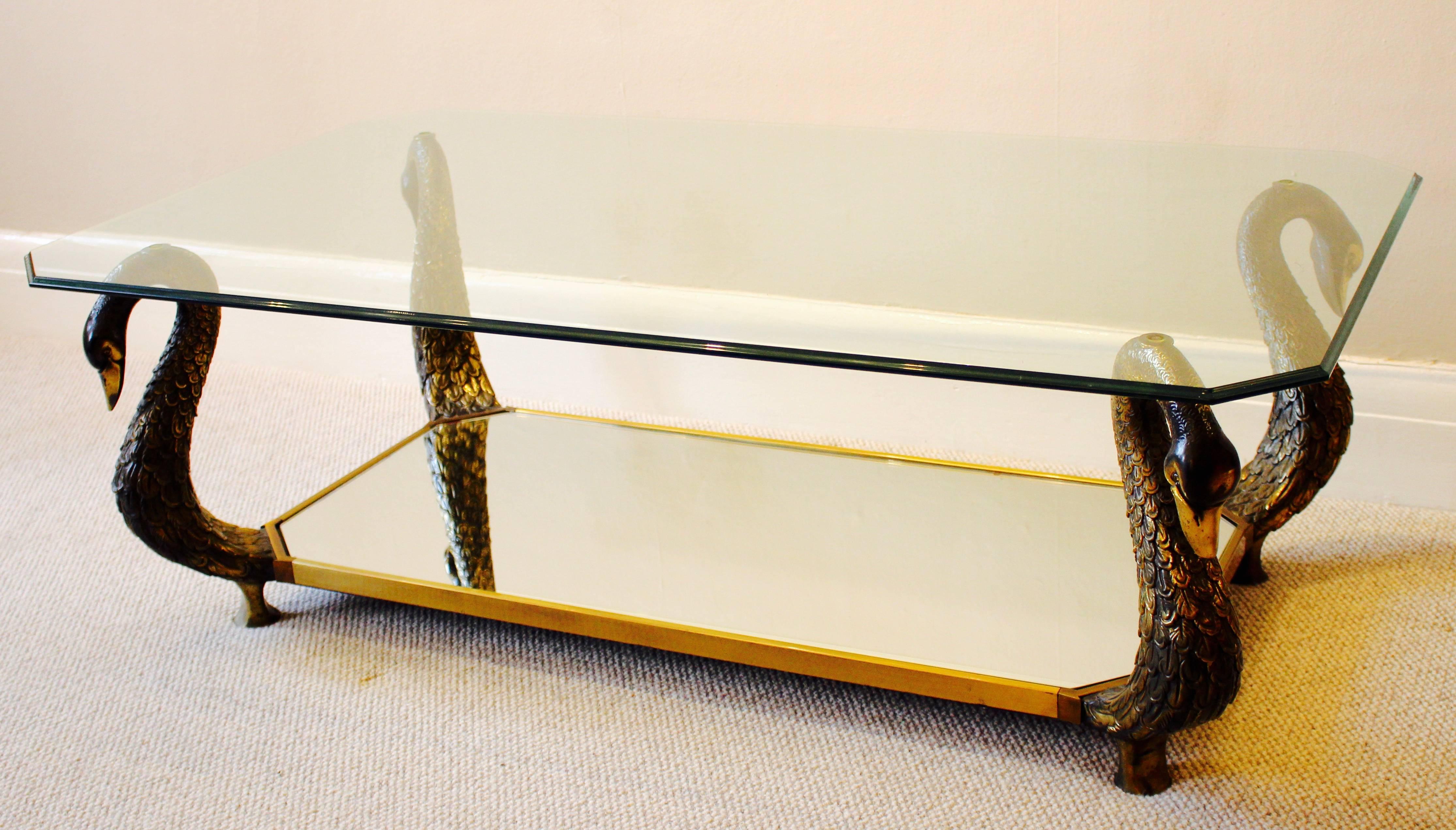 A stylish and highly decorative French gilt bronze swan-neck coffee table. Rectangular tempered glass top with canted corners. Supported by faded gilt bronze swan necks with mirror shelf below and being framed in brass trim. A beautiful piece that