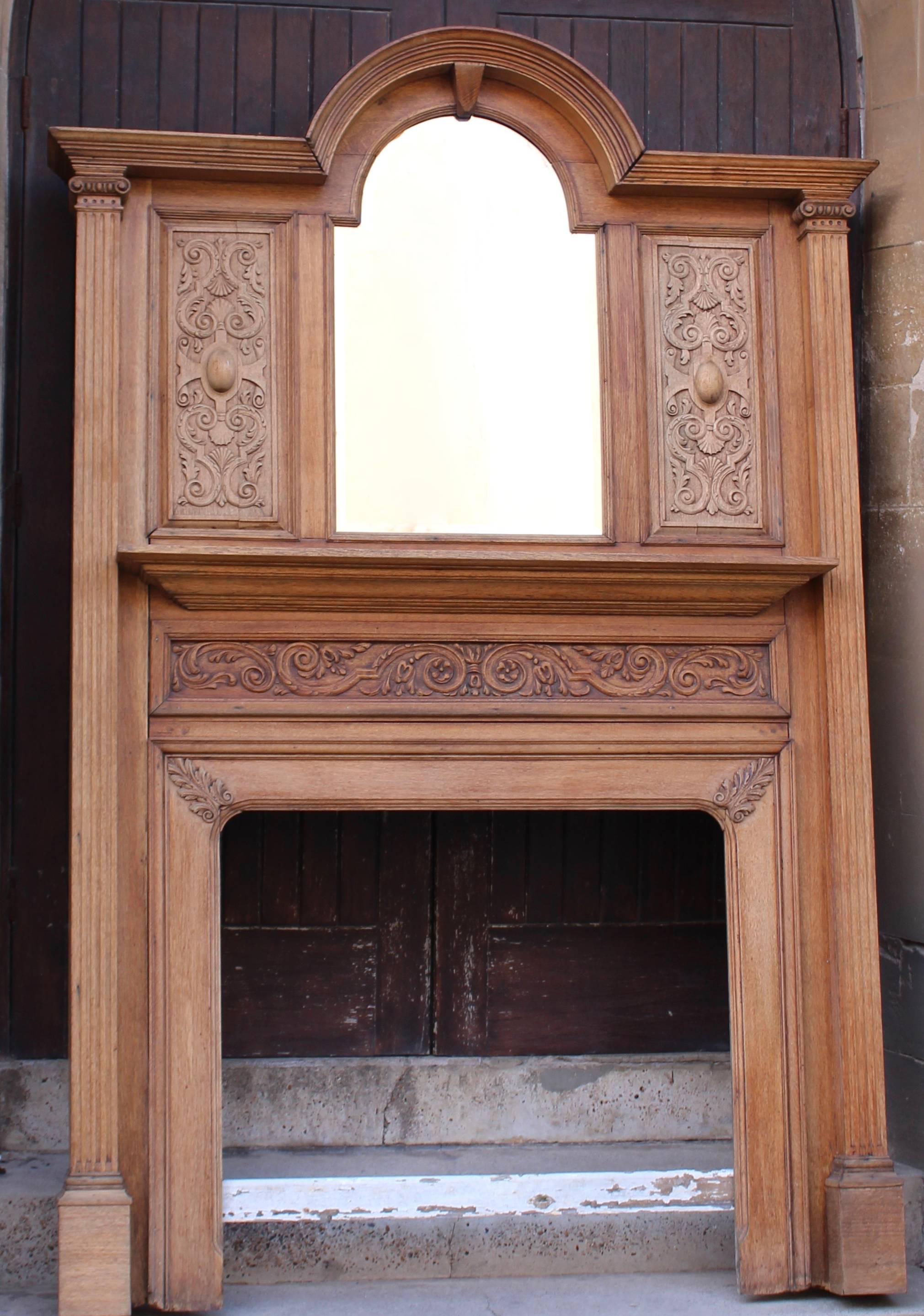 A handsome and imposing carved oak fireplace standing at over eight feet tall. Having a stepped and domed cornice. Arched and bevelled mirror to centre flanked by beautifully carved panels. Each having hand carved swags and tail decoration with