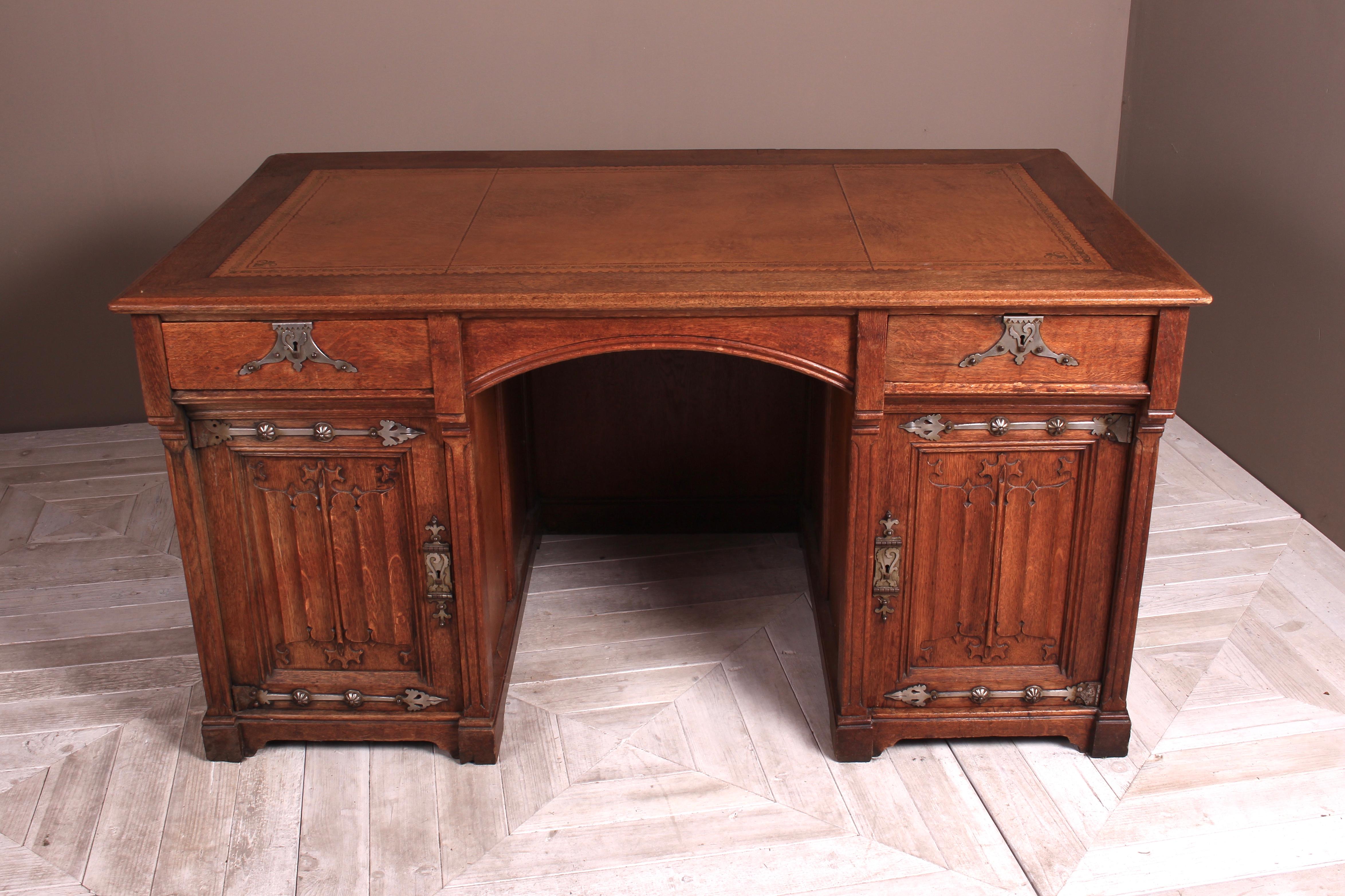 A beautiful Victorian Gothic Revival oak desk in the manner of Pugin, circa 1880. The desk having a tooled tan leather writing top above a central arched kneehole opening. Flanked to each side by drawers and cupboards with enclosed shelf. The doors