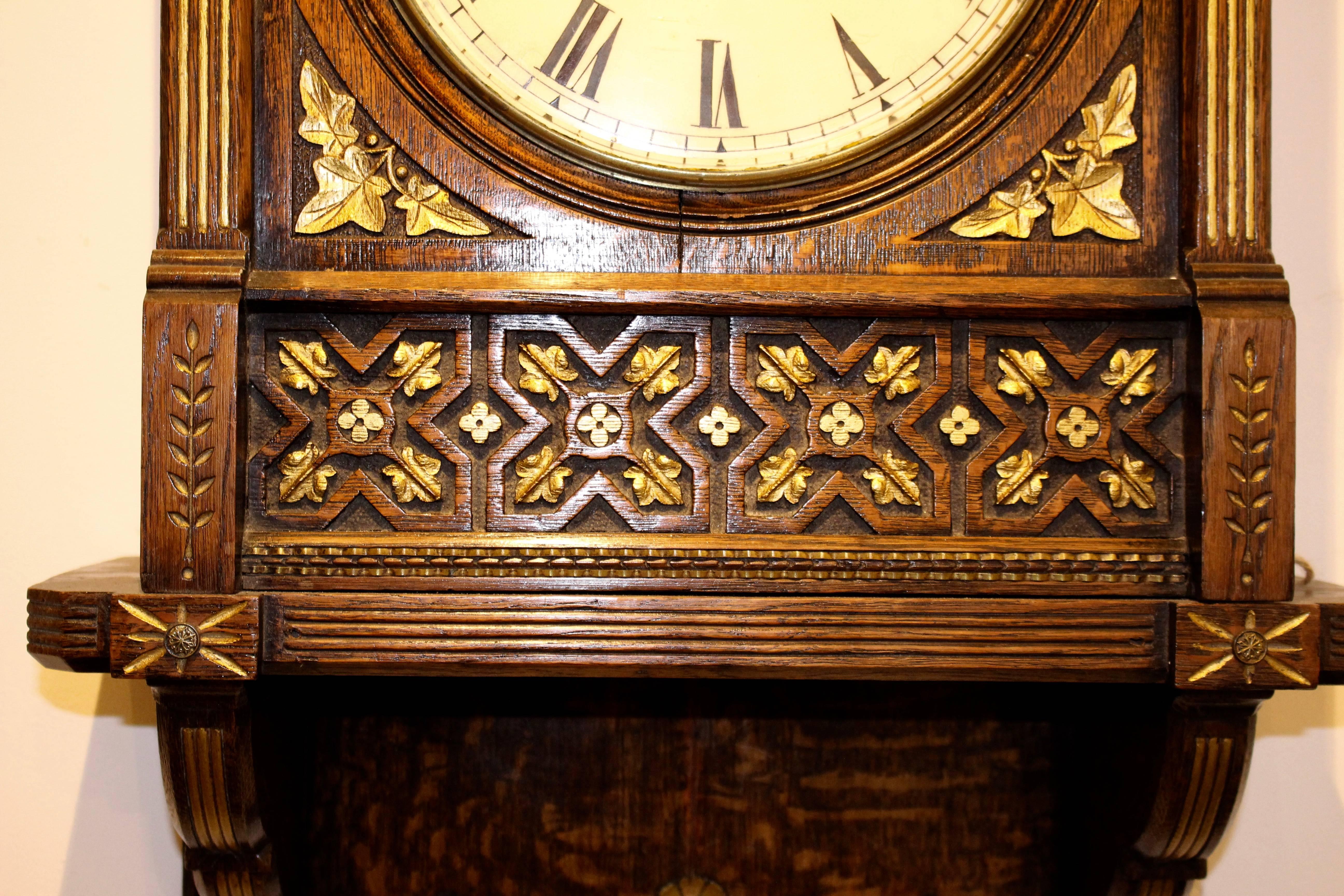 A beautifully crafted oak clock in the Gothic Revival manner from the Victorian era. Eight-day double fusee movement. The central enamel Roman numeral face enclosed by a glass case.
To each corner, we have carved gilt leaf decoration. They are