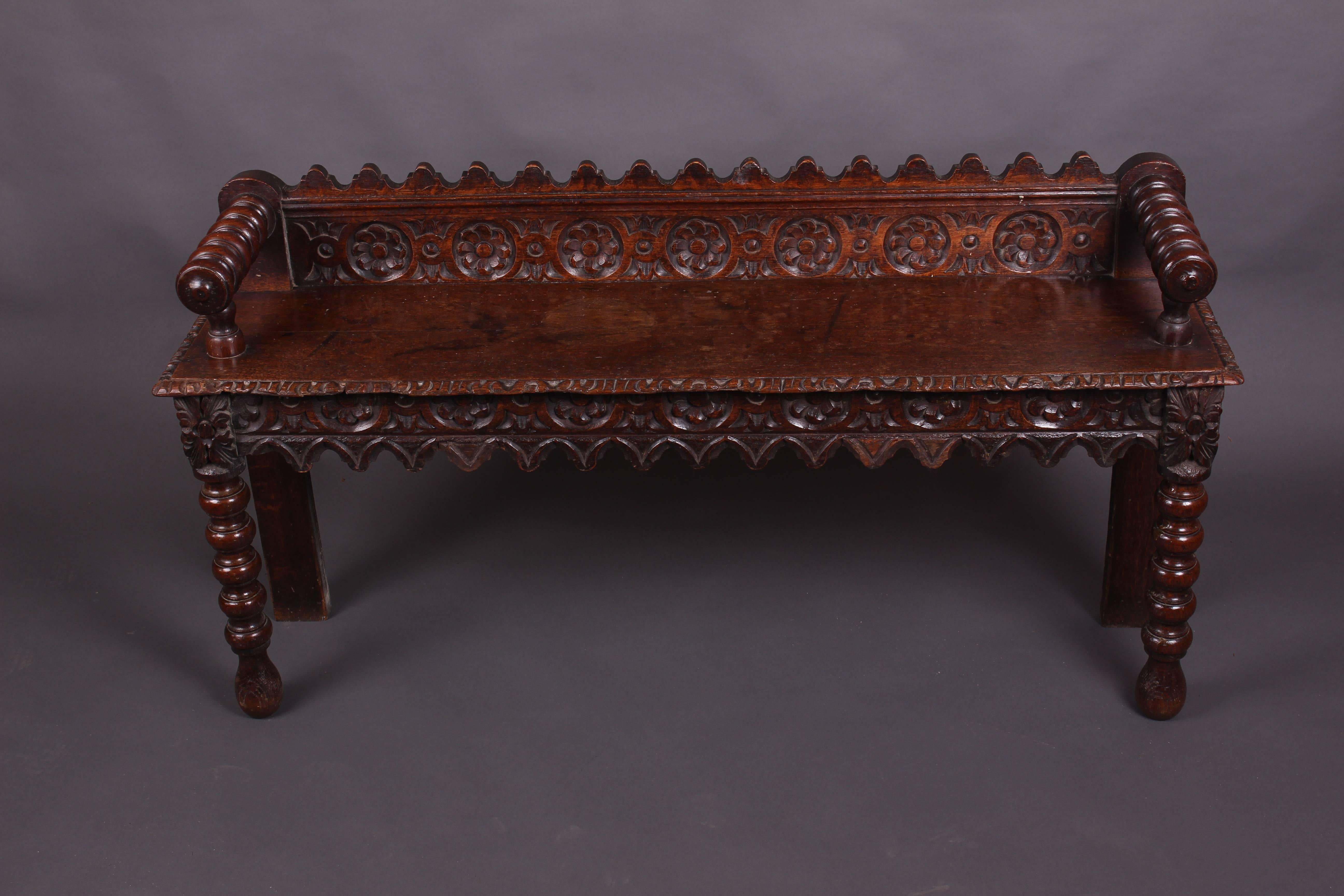 An attractive Victorian Oak window seat having Gothic style rosette carvings on the back rail and front skirt. Pretty Egg and Dart carving to the seat lip. Turned armrests and front legs terminating on bun feet. An all round functional and good