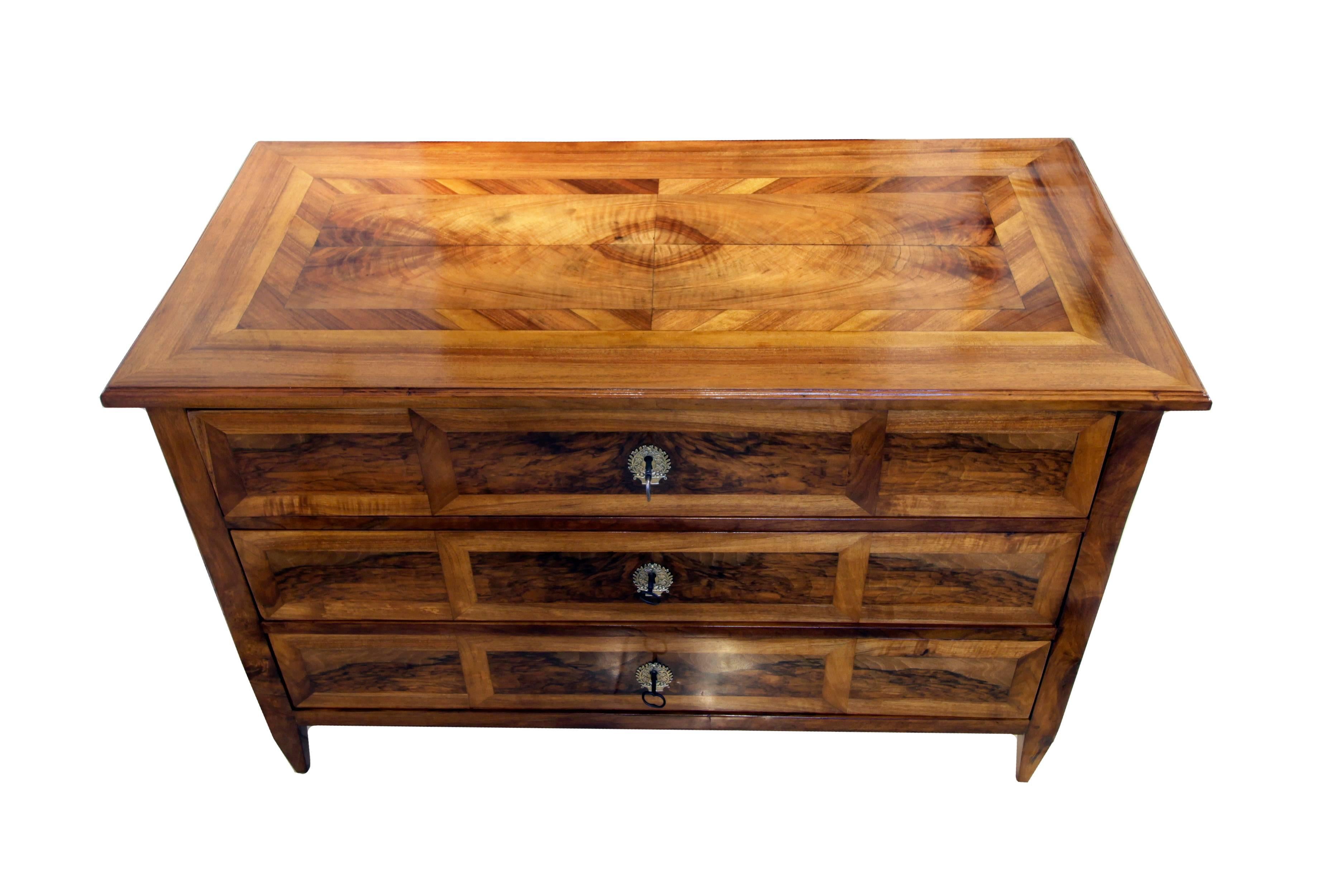 An 18th century Louis XVI marquetry commode with three drawers was build in south Germany. The veneers of walnut and inlaid with other walnut on a pinewood corpus. All locks, fittings and the key are original. The feet are tapered square. It is a