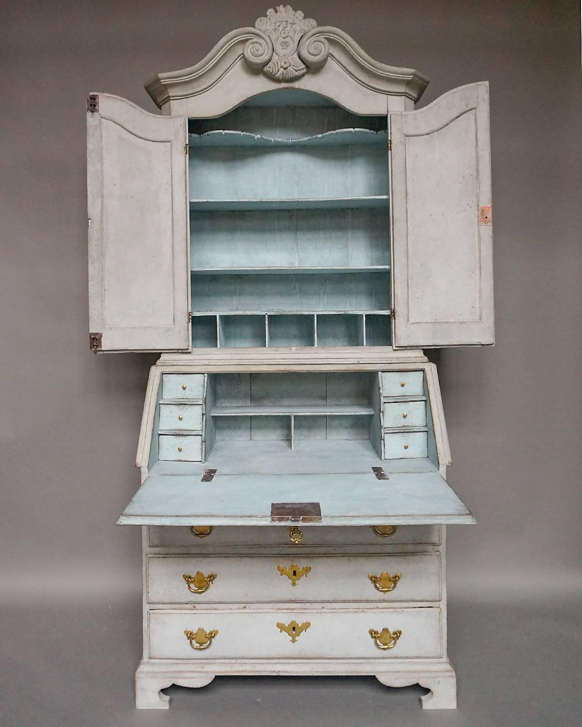 Early Swedish Baroque secretary in two parts dated 1734. The upper section has two doors with raised panels under a scrolled broken pediment with central dated plaque with floral carving. Inside are four fixed shelves, the top one shaped and notched