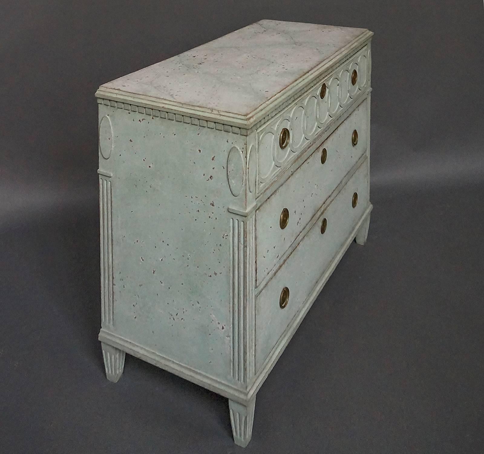 Swedish chest of drawers, circa 1860, in pale green paint with faux marble top. A frieze of interlocking rings on the front of the top drawer, dentil molding around the top, and reeded corner posts with raised ovals at the top. Tapering square legs