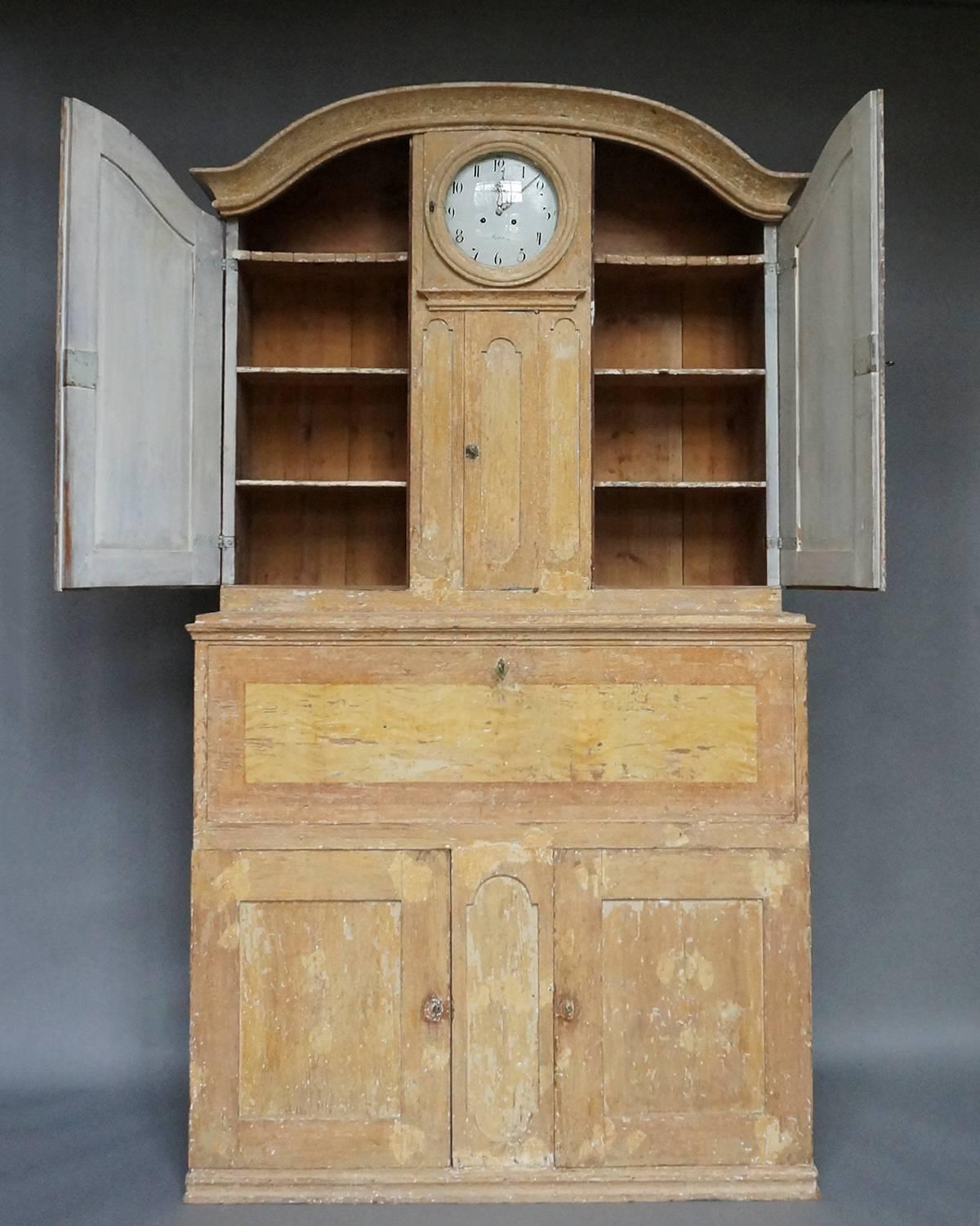 Period secretary from Hälsingland with integral Mora clock and with original paint, Sweden, circa 1840. On either side of the clock is a cabinet with arched doors and three interior shelves. Behind the fall front are two banks of three drawers each.