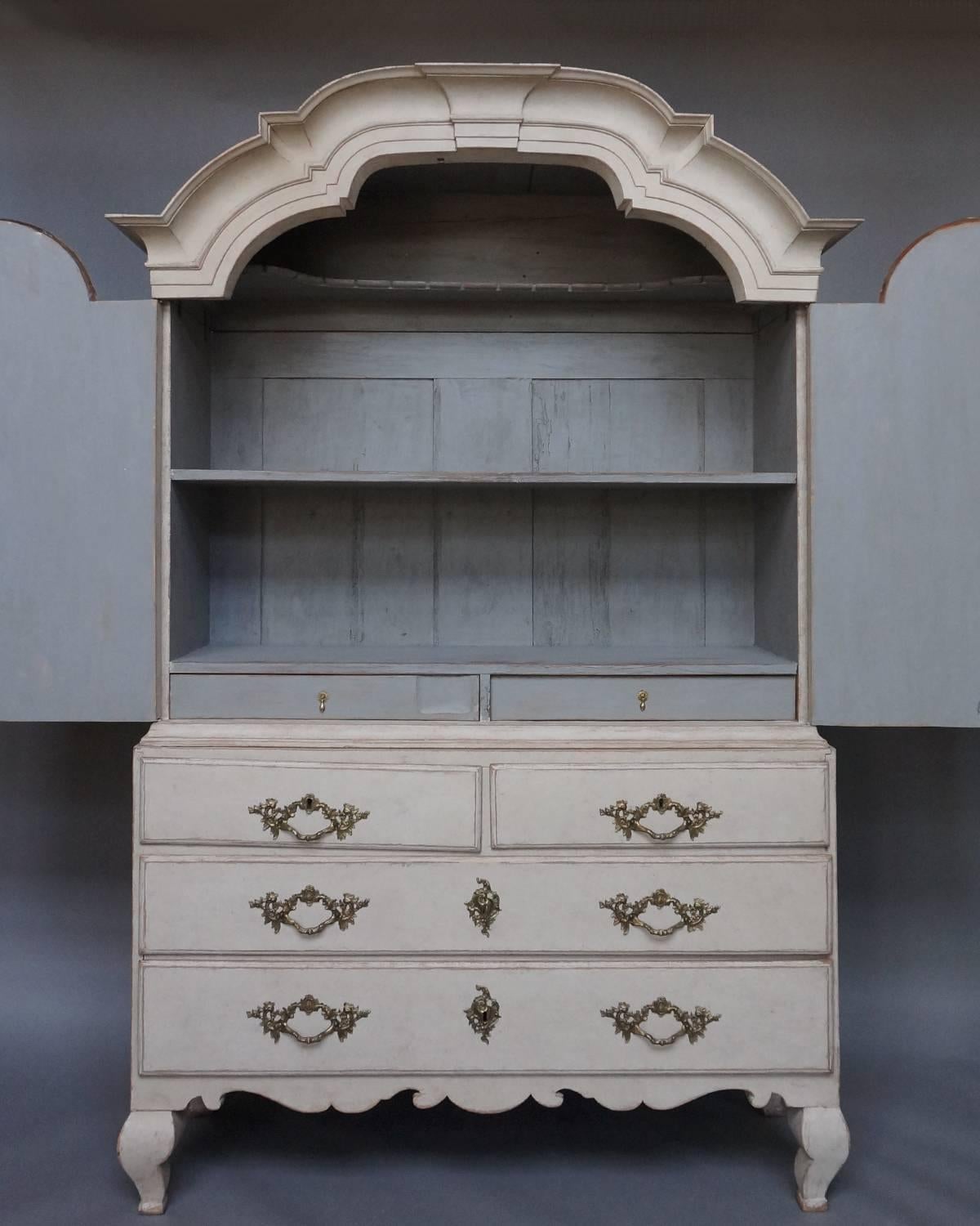 Swedish Baroque cabinet in two parts, circa 1760, with original hardware. The upper section has two shelves and two drawers behind double doors, all under an arched cornice. The lower section has two over two drawers on a shaped base with compressed