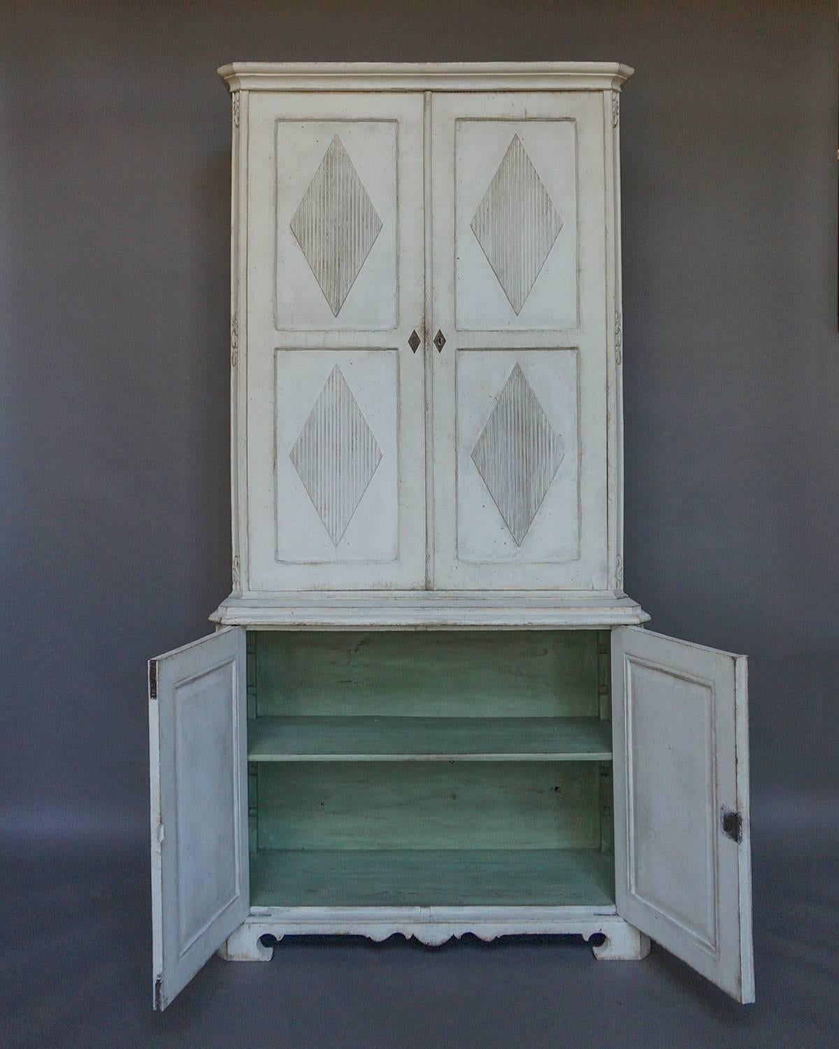 Cabinet in two parts, Sweden circa 1800.  The tall upper section has double doors, each with two reeded lozenges, which open onto two shelves, three small drawers, and 28 compartments.  The deeper lower section has two shelves behind double doors,
