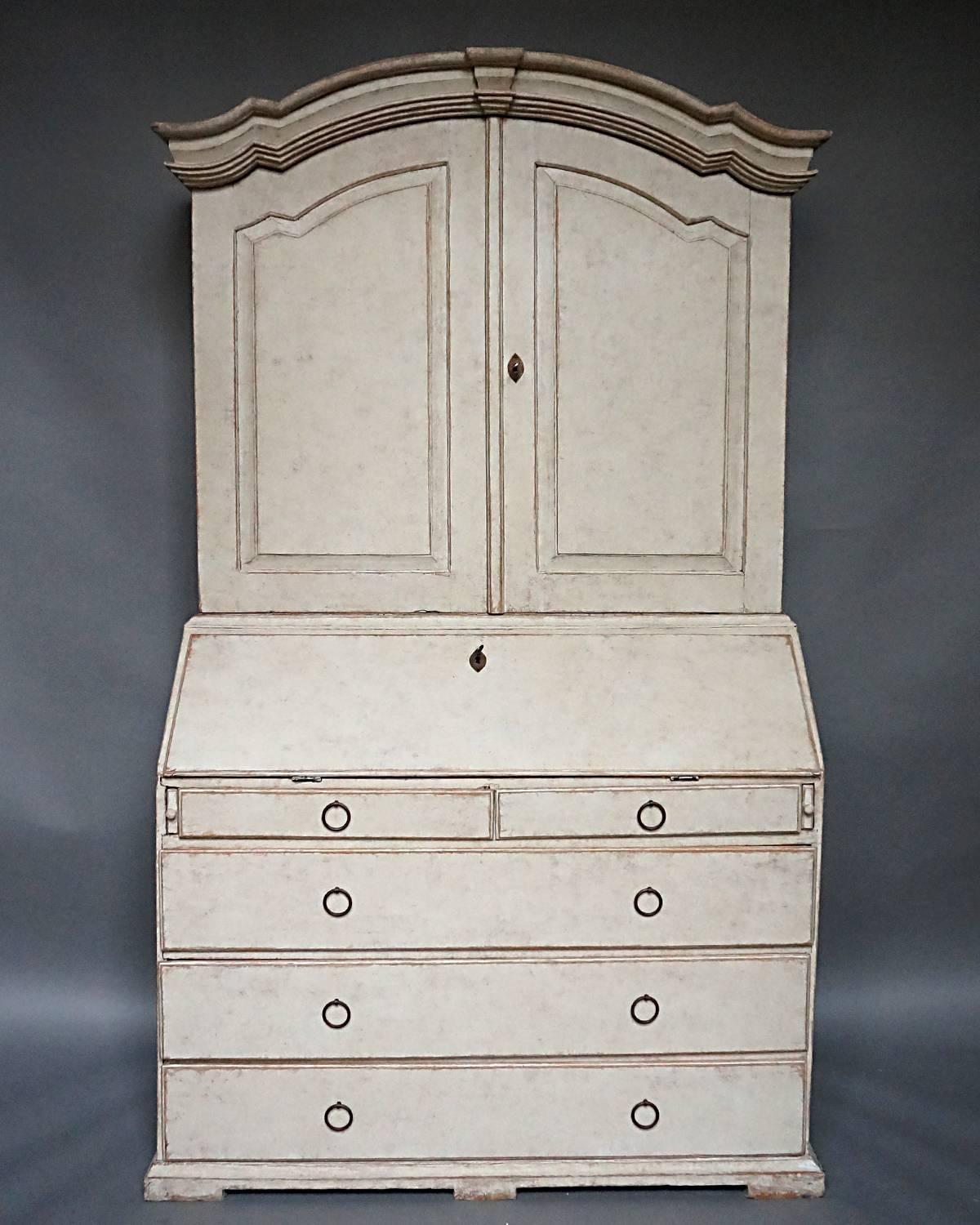 Period Baroque secretary, Sweden, circa 1800, in two parts. The library section has an arched cornice with keystone detail over raised panel doors. The interior has three fixed shelves, the top shaped for spoons.

The lower section has a fitted