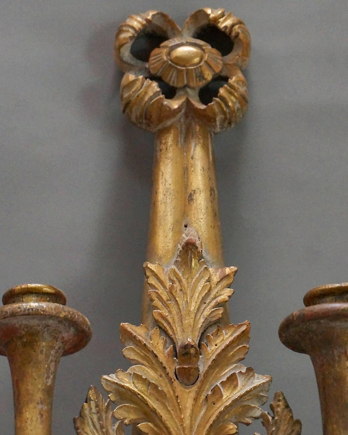 Pair of gilt sconces from the Swedish Empire period, circa 1830. Each piece is carved to represent a tasselled ribbon hung from a floret and tied with a cluster of acanthus leaves. Two trumpet shaped candle holders on each.