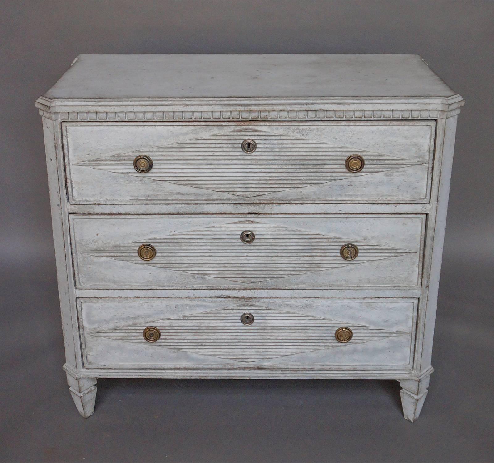 Swedish chest of drawers in the Gustavian style, circa 1850. Three drawers, each with a raised and reeded lozenge and brass hardware. Shaped top, dentil molding, and canted corners.