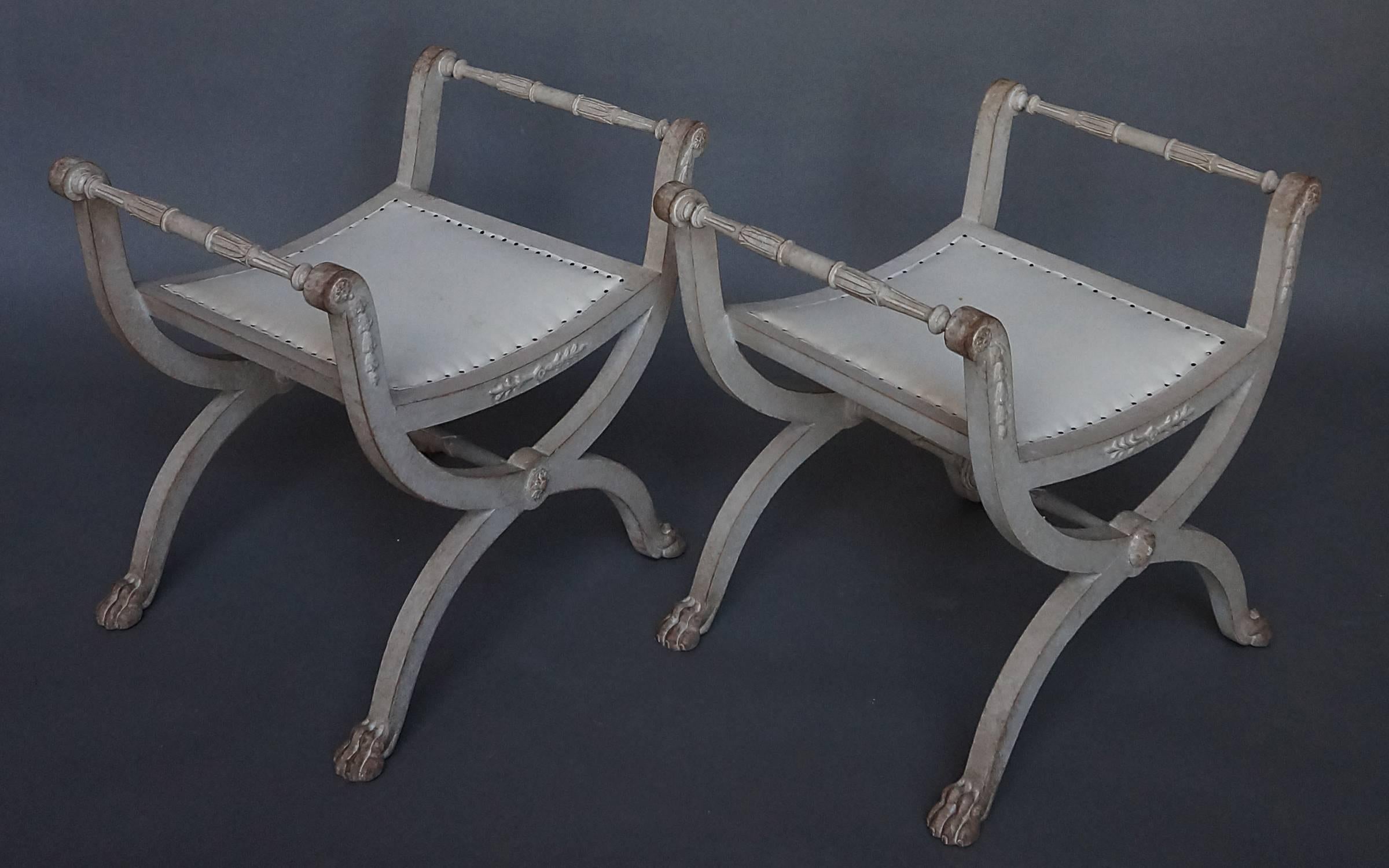 Pair of Swedish Curule stools, circa 1900, in the Gustavian style. Carved bellflowers on the arm supports, and lotus carving on the stretchers. Lions paw feet.