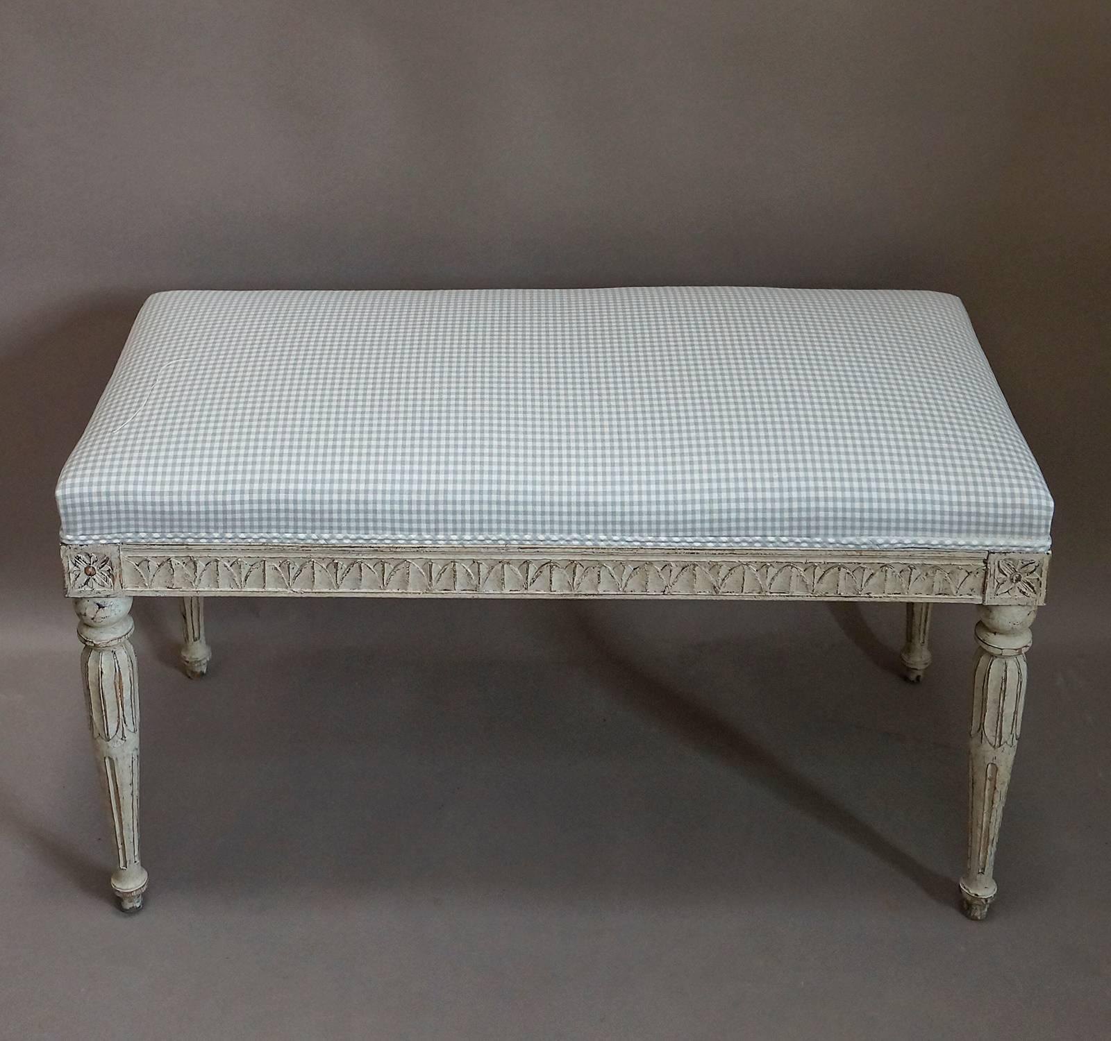 Swedish bench in the Gustavian style, circa 1900. Lamb’s tongue molding on the apron with florets at the corner blocks. Tapering round legs with lotus blossom carving at the top.