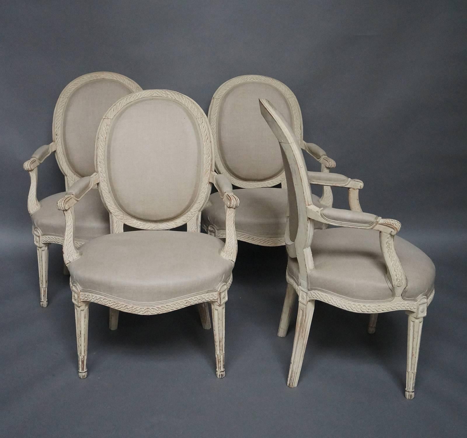 Set of four antique Swedish chairs in the Gustavian style, circa 1870, with guilloche carving surrounding the backs and repeating on the armrest supports and the apron. Upholstered seats, backs, and armrests. Tapering, square legs.