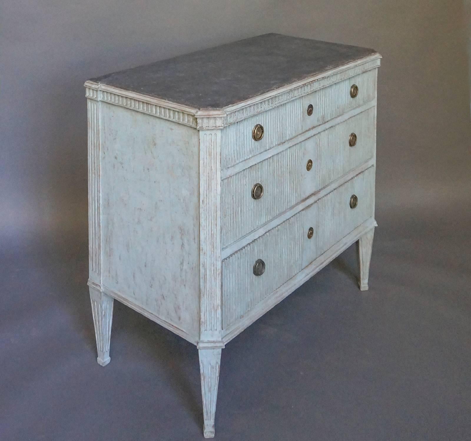 Swedish three-drawer chest, circa 1850, in pale blue paint. Vertical reeding on the drawer fronts and dentil molding under the black-painted top. Canted corners with vertical reeding on the corner posts and tapering, square legs. Original brass