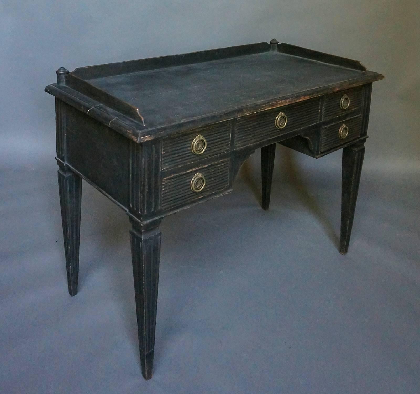 Black painted knee hole writing desk, Sweden, circa 1860. The top has a gallery edge with turned posts at the back corners as a decorative flourish. The five drawers have horizontal reeding, as do the tapering square legs. Quite a nice look to this
