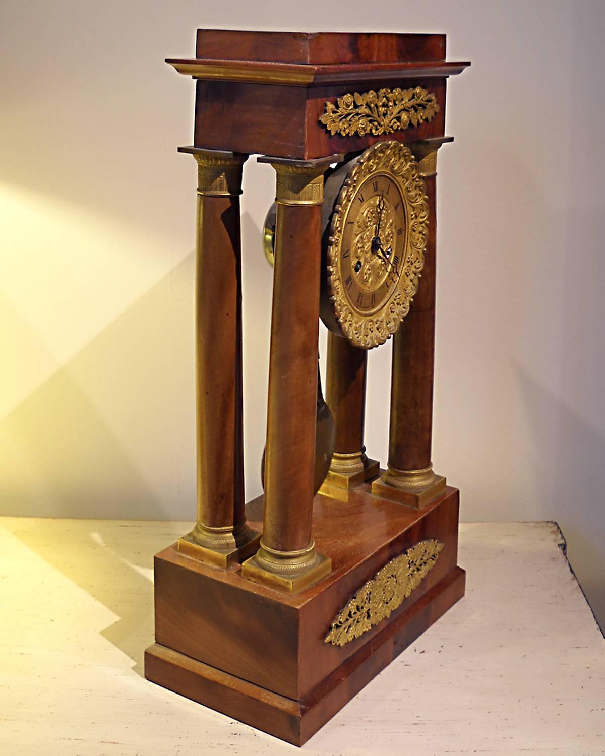 French Charles X portico clock with flame mahogany veneers and gilt bronze mounts. Supported by four Egyptian columns. Roman counters on the gilt face and center and a brass drop pendulum, 19th century. (Price reduced from $3,200.).