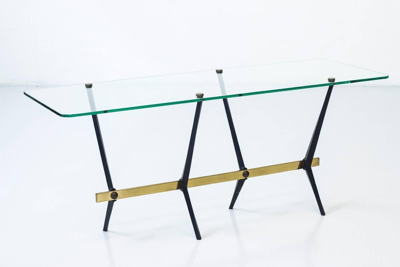 Sculptural coffee table designed by Angelo Ostuni most likely made in Italy during the 1950s. Thick glass top with rounded corner, supported by a brass and black lacquered metal frame/ legs. Very good condition with signs of wear and age related