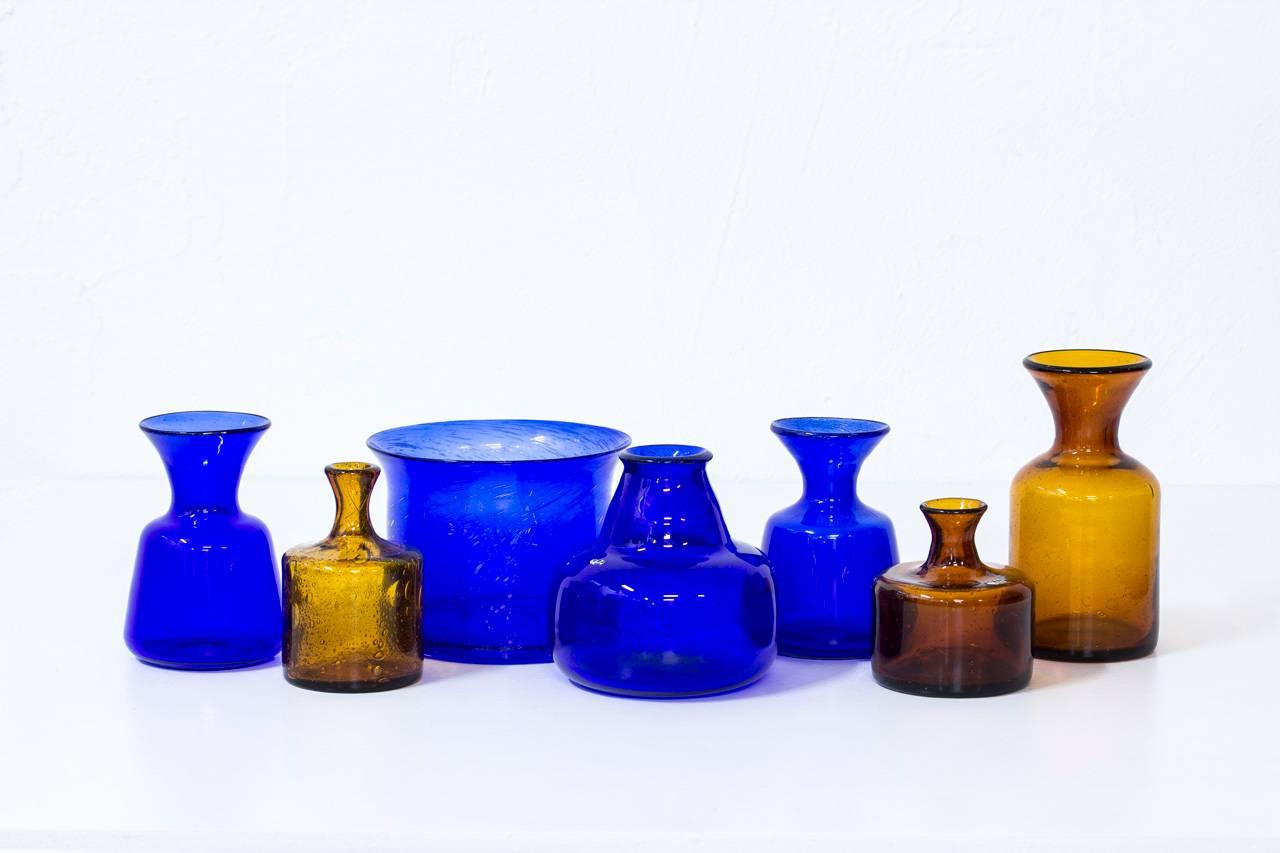 Group of seven glass vases designed by Erik Höglund, handblown at Boda glassworks in Sweden during the 1950s. Collection of blue and amber vases of various sizes and shapes, all with bubbles in the glass. Five of the vases are engraved with