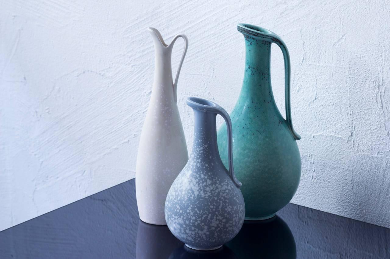 Set of three stoneware jugs/ vases by Gunnar Nylund for Rörstrand. Handmade in Sweden during the 1940s and 1950s. First vase with a matte blue speckled grey glaze. Second one in speckled white glaze. Third one in jade color speckled grey. Hand