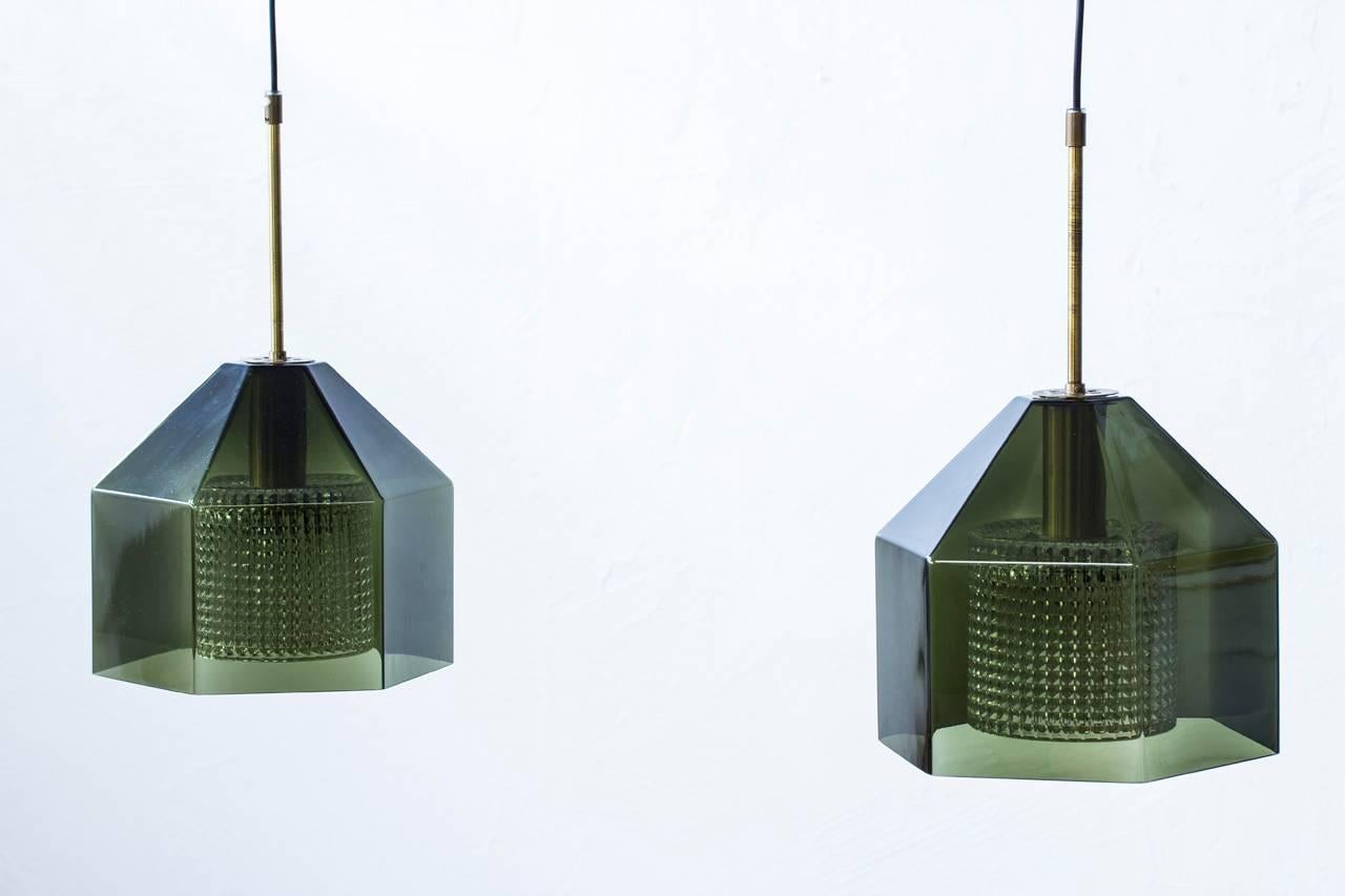 Pair of pendant lamps designed by Carl Fagerlund for Swedish glass company Orrefors during the 1960s. Hexagon, shaped cup of green tinted glass with internal diffuser in clear pressed glass. Brass fittings and new electricity. Excellent condition