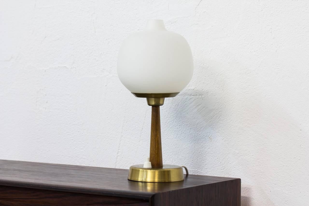 Table lamp designed by
Hans Bergström. Produced
by his own company Ateljé
Lyktan in Åhus, Sweden
during the 1950s. Stained
beech stem with polished
brass base and support.
Opaline glass shade. Light
switch on the base.