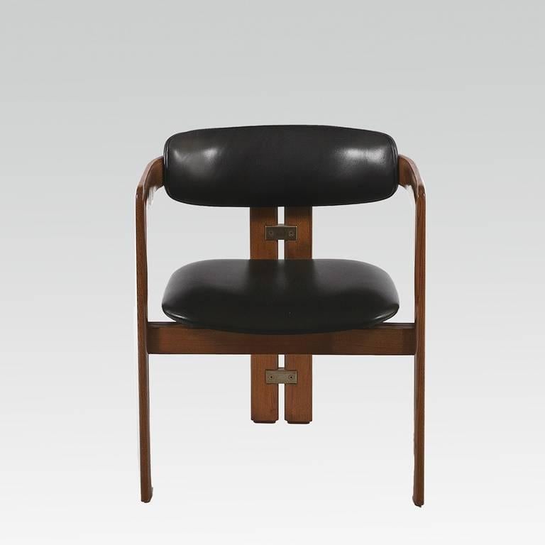Set of eight Italian midcentury, teak, barrel shaped dining chairs designed by Augusto Savini in 1965 for Poggi. Back support and seat in black leatherette; double back legs interlinked with two sets of brass plates.