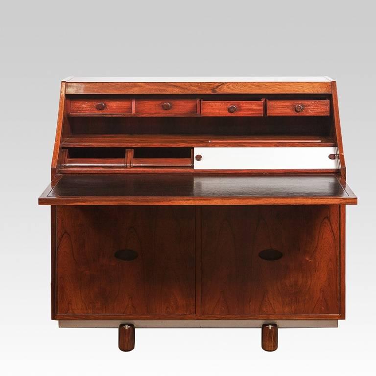 Beautiful Italian rosewood, tambour fronted, writing desk resting on two pairs of stylized pedestal legs. The pull-out writing surface is covered in black leather with four drawers overhead and four trays concealed behind two sliding, brushed steel,