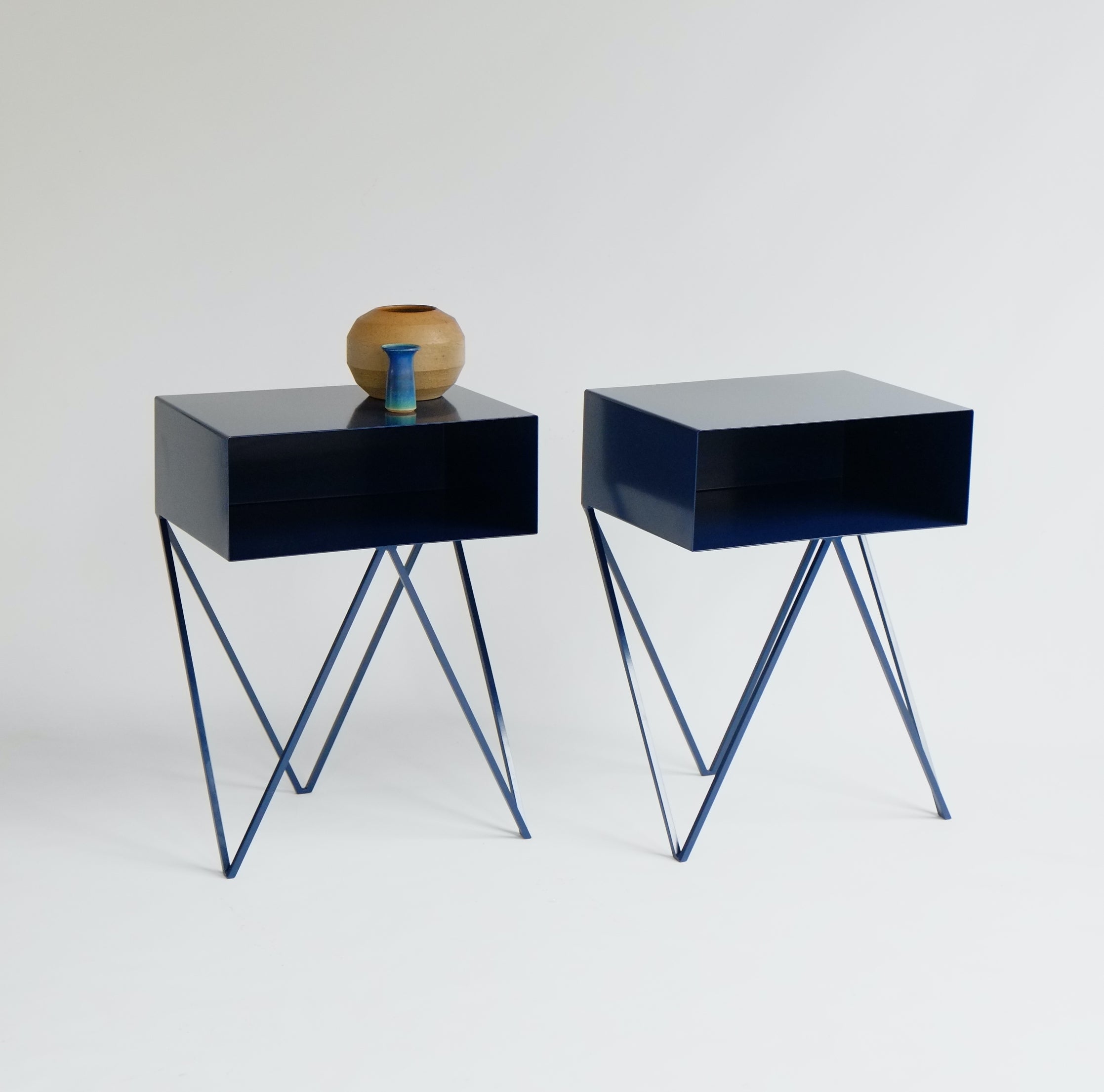 A pair of nightstand tables. 

The Robot side tables feature an open shelf on zig zag legs. A fun and functional design made of solid steel, powder-coated in dark blue. The clean lines look great against period details as well as in modern spaces.
