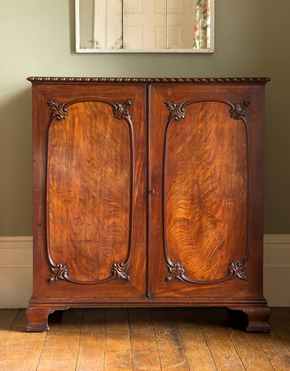A fine and rare Gentleman's Press, the solid timber top with gadrooned edge sits above a pair of rectangular doors inset with beautifully figured flame mahogany veneer panels carved in each corner with scrolling leaf decoration in the Rococo style.